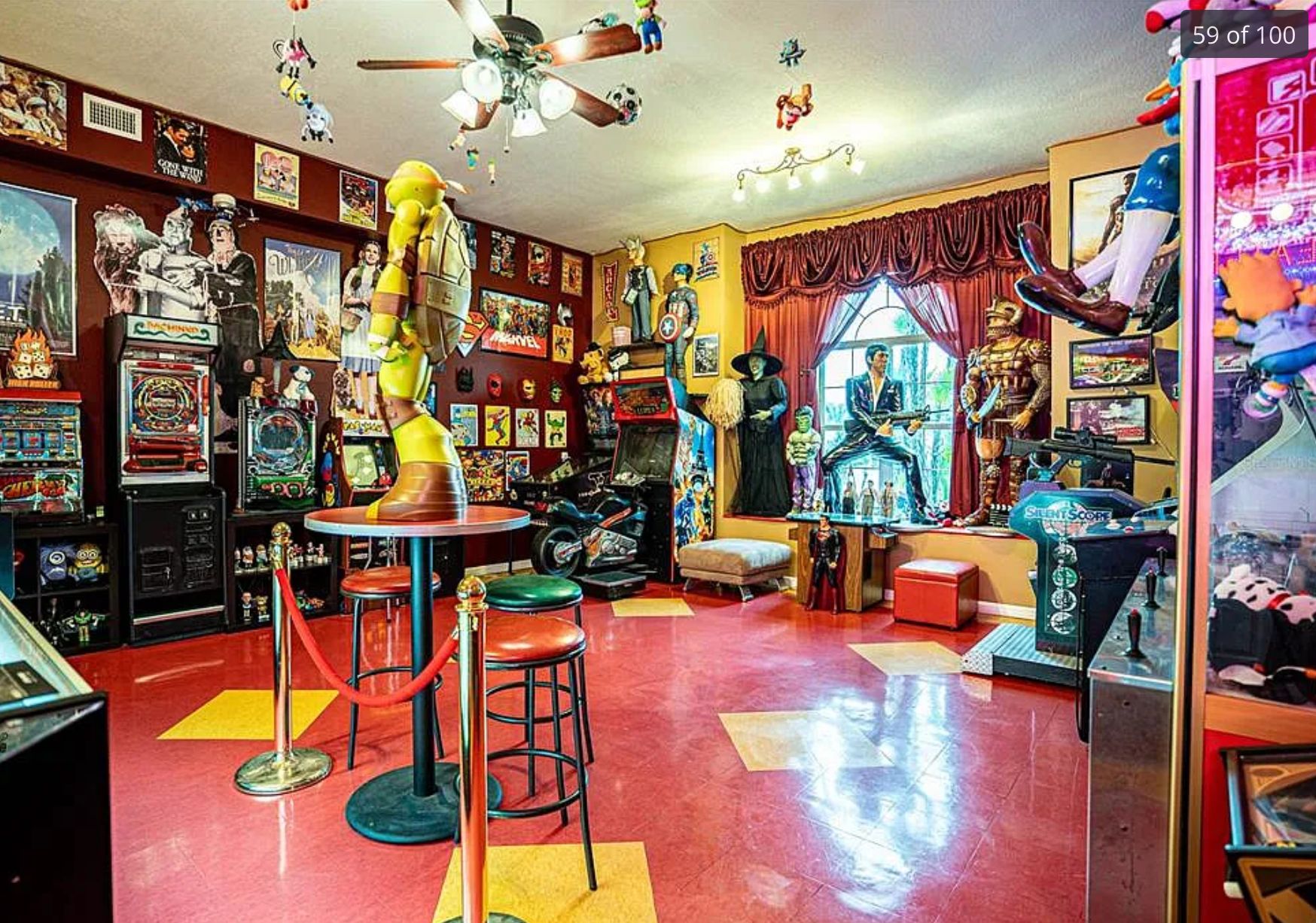 A room with a red shiny floor with yellow diamonds, and it is also full of stuff. There is a small round table in the middle with a huge statue of a Ninja Turtle. There are jukeboxes and slot machines and Wizard of Oz themed items such as a scale model of the Wicked Witch of the West. 