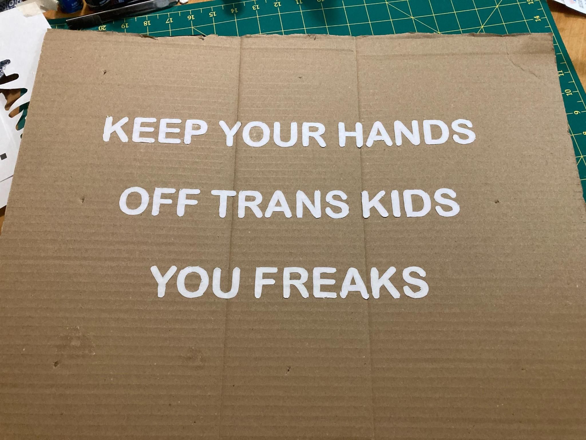 A cardboard protest sign that says "Keep your hands off trans kids you freaks"