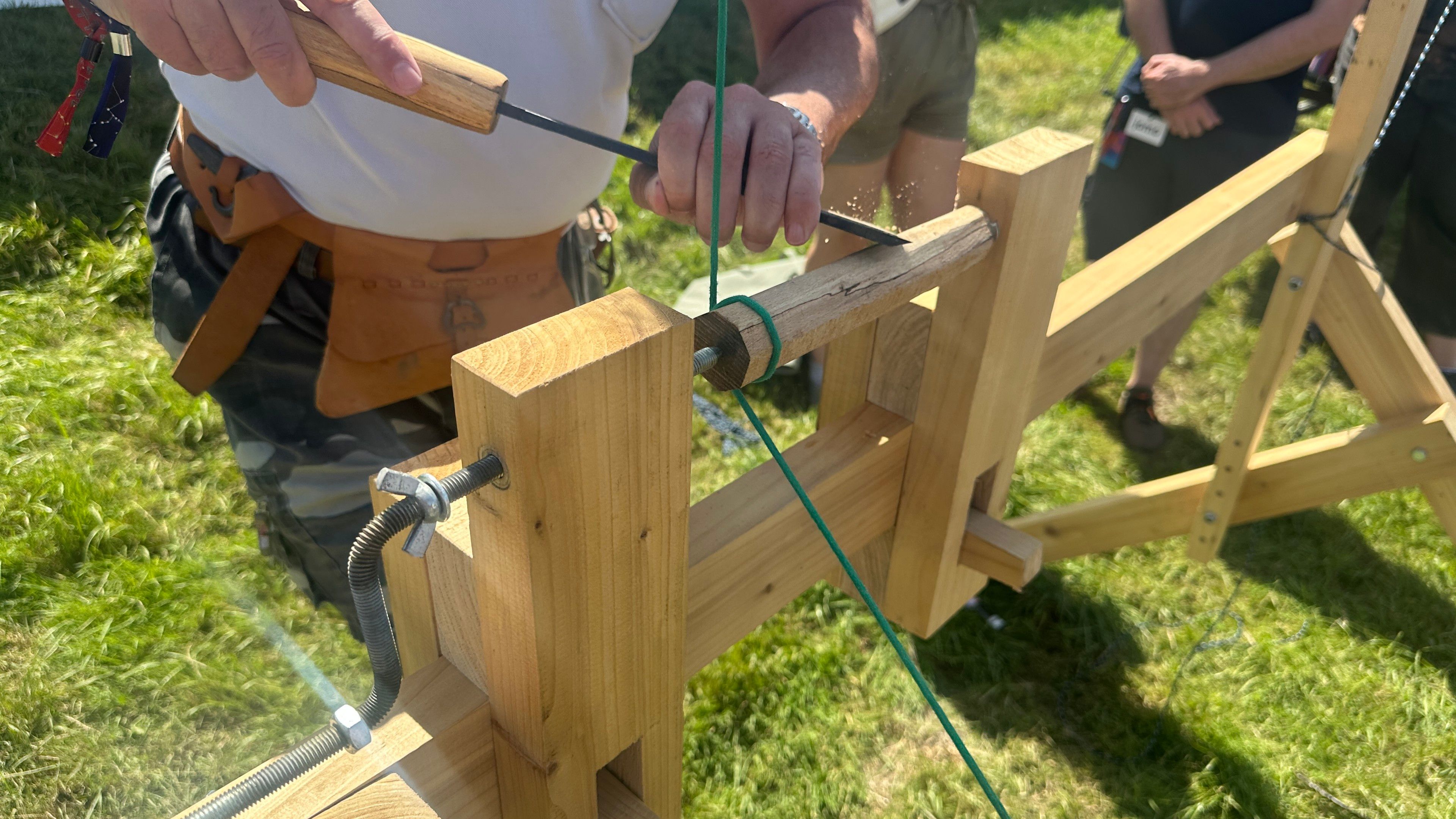 Person holding a wide chisel against a small piece of wood on a foot operated spring lathe. 