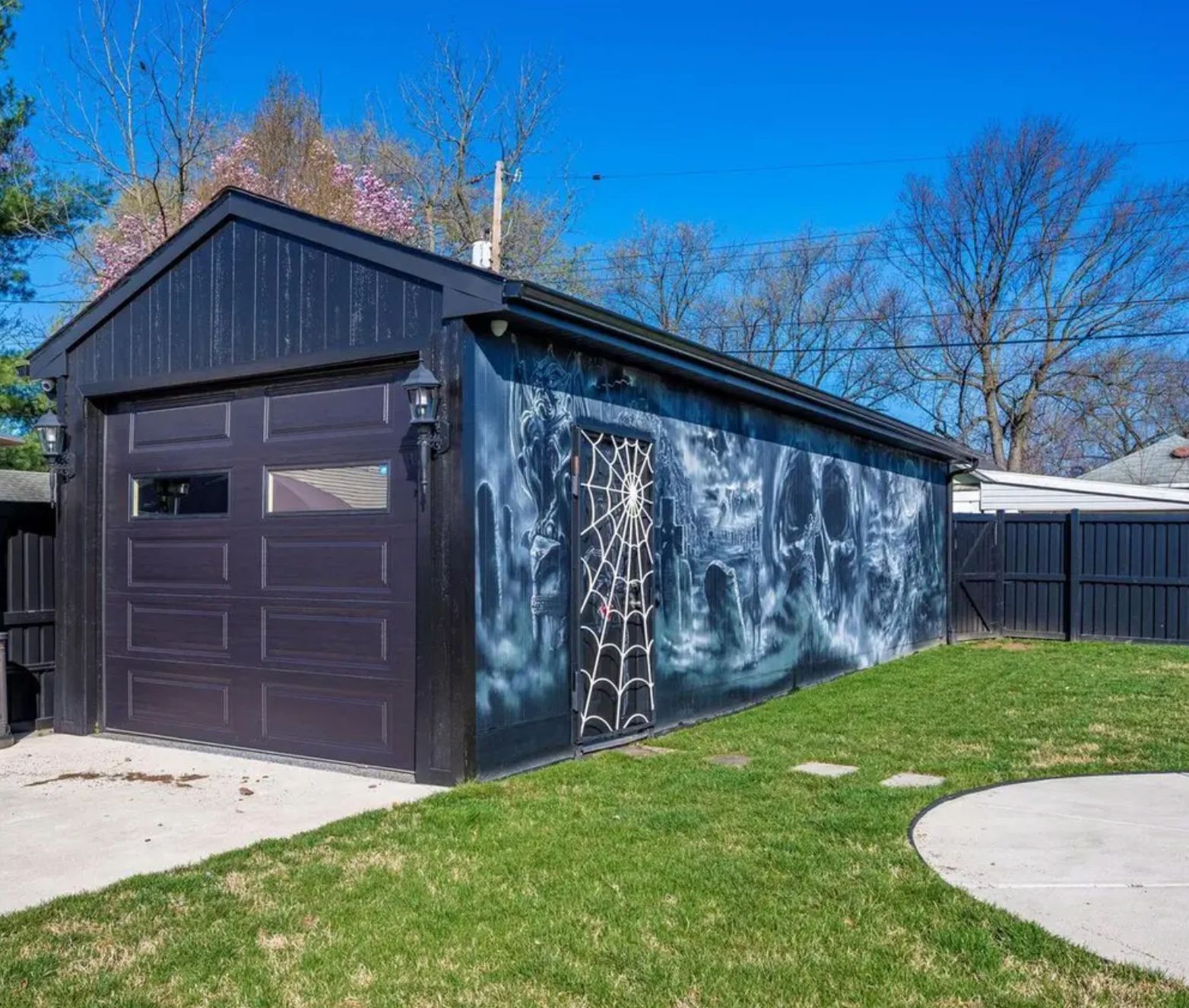 The garage in the backyard and there is a mural on the side that's blue and swirly and has a skull. The side door also has a spider web painted on it. 