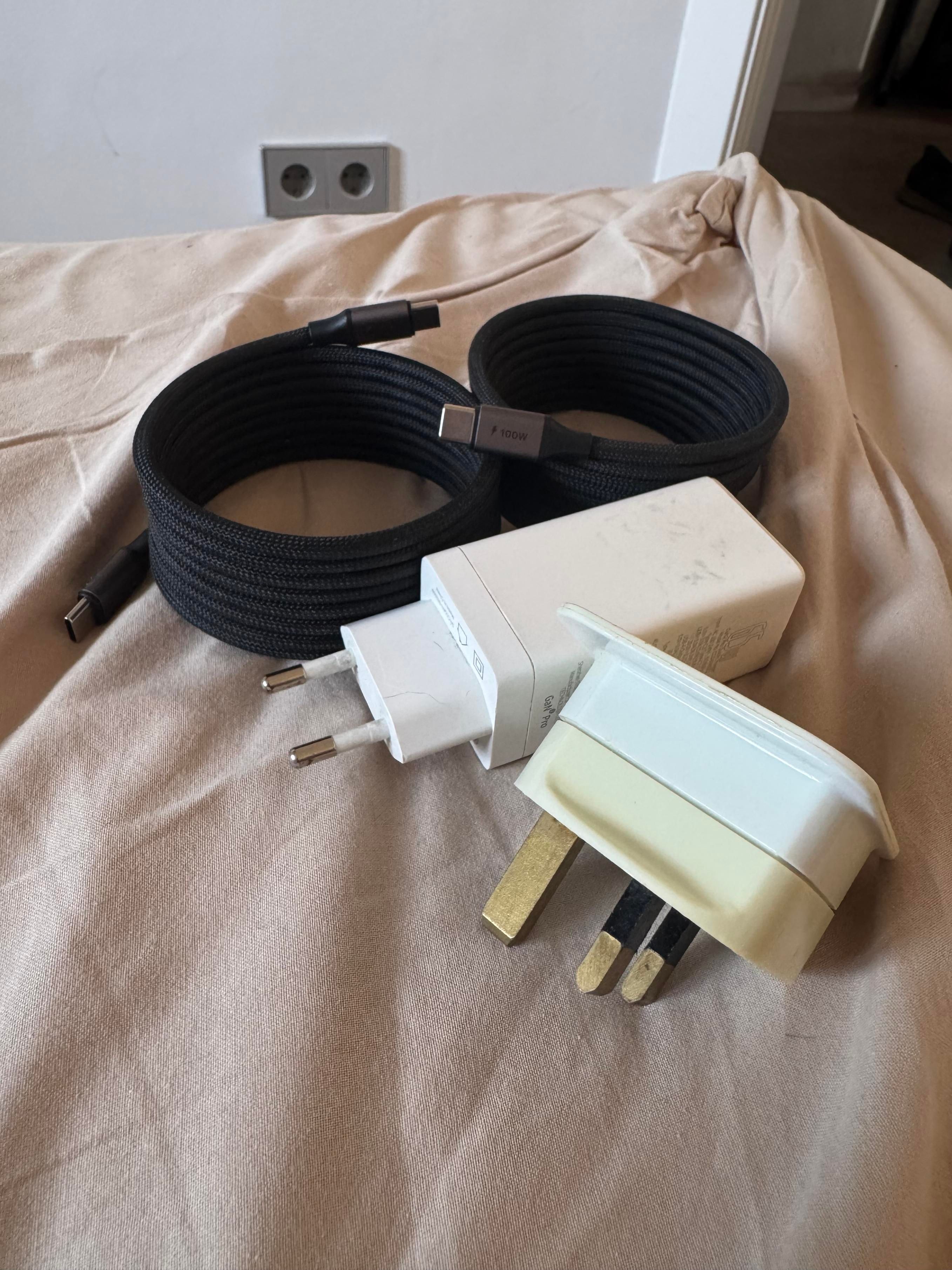 Packing preparation on a bed, two coiled USB-C cables, a European power brick and a somewhat yellowed UK-European plug adapter 