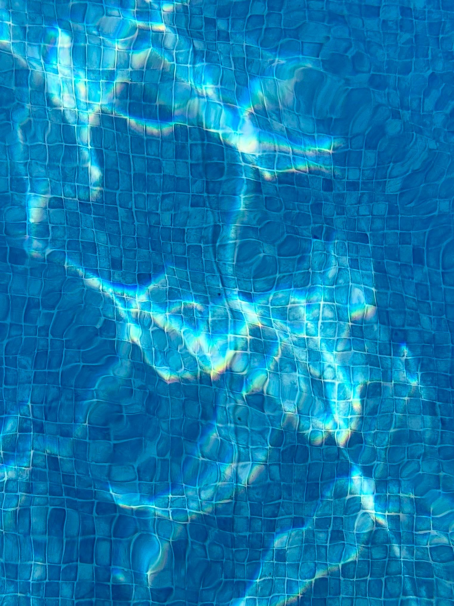 Light caustics in a pool, bright ribbons of fluctuating light, with a distorted blue tile pattern at the bottom. 