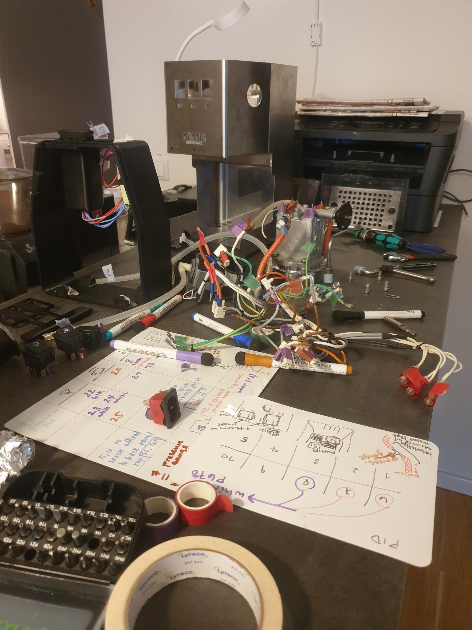 Fully disassembled Gaggia Classic espresso machine is now piecewise across the kitchen counter. Notes on paper-sized whiteboards about what connects where are near the foreground. A hydra of wires, each labeled at both ends, is near the middle. Behind that are the boiler, tubing, and the metal shell of te machine.
