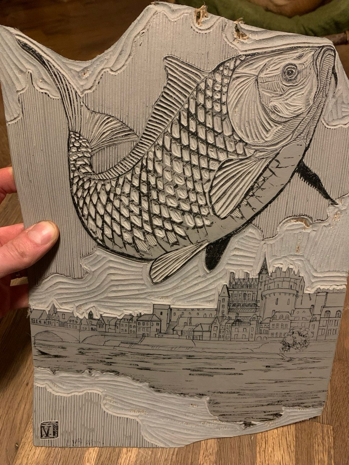 Gravure en cours sur une plaque de linoléum: une grosse carpe saute avec en arrière-plan une ville et un château en bord de fleuve