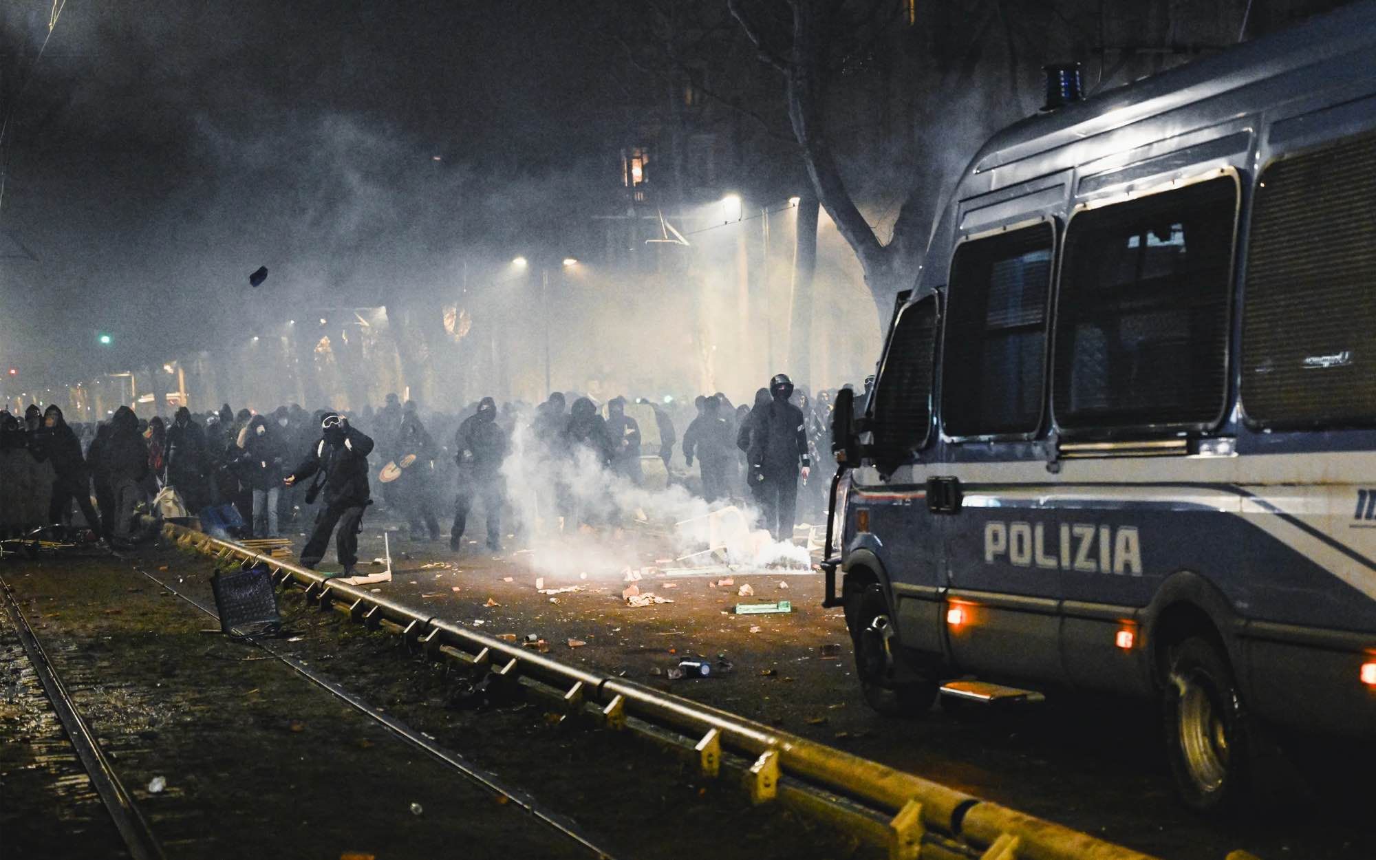 A photograph of the Corso Regina Margherita in Turin on the evening of January 31, 2026, showing protesters facing off against a police van.