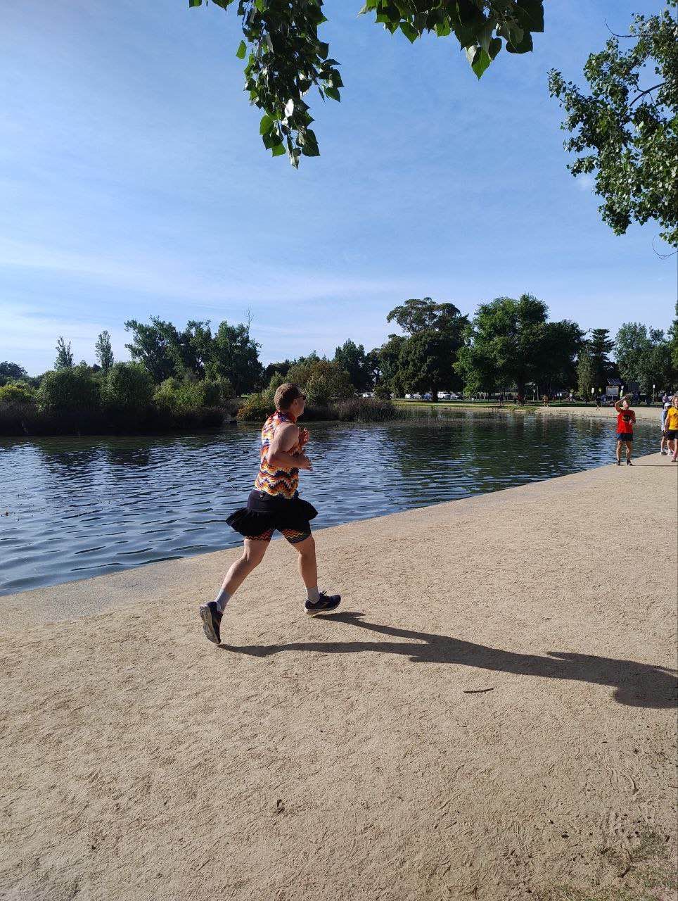 Picture of me side-on running Parkrun in pride color shorts and a black miniskirt
