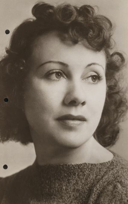 Doris Patston, from a photo in the New York Public Library Digital Collections; a white woman with curly ark hair, wearing a sweater with a boat-style neck