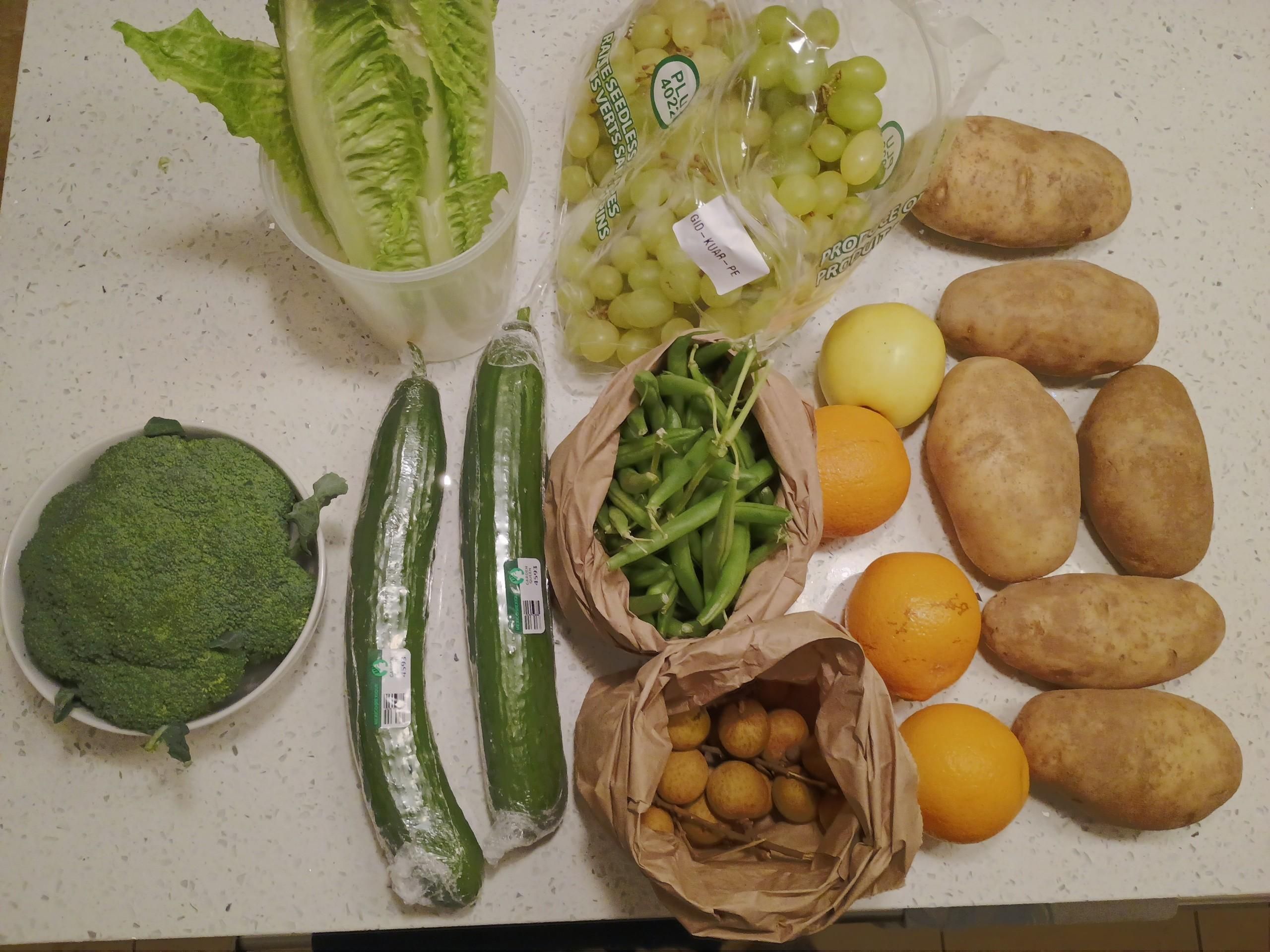 An array of vegetables and fruit. Lettuce, grapes, potatoes, oranges, an apple, , broccoli, green beans, and unknown brown marbles.