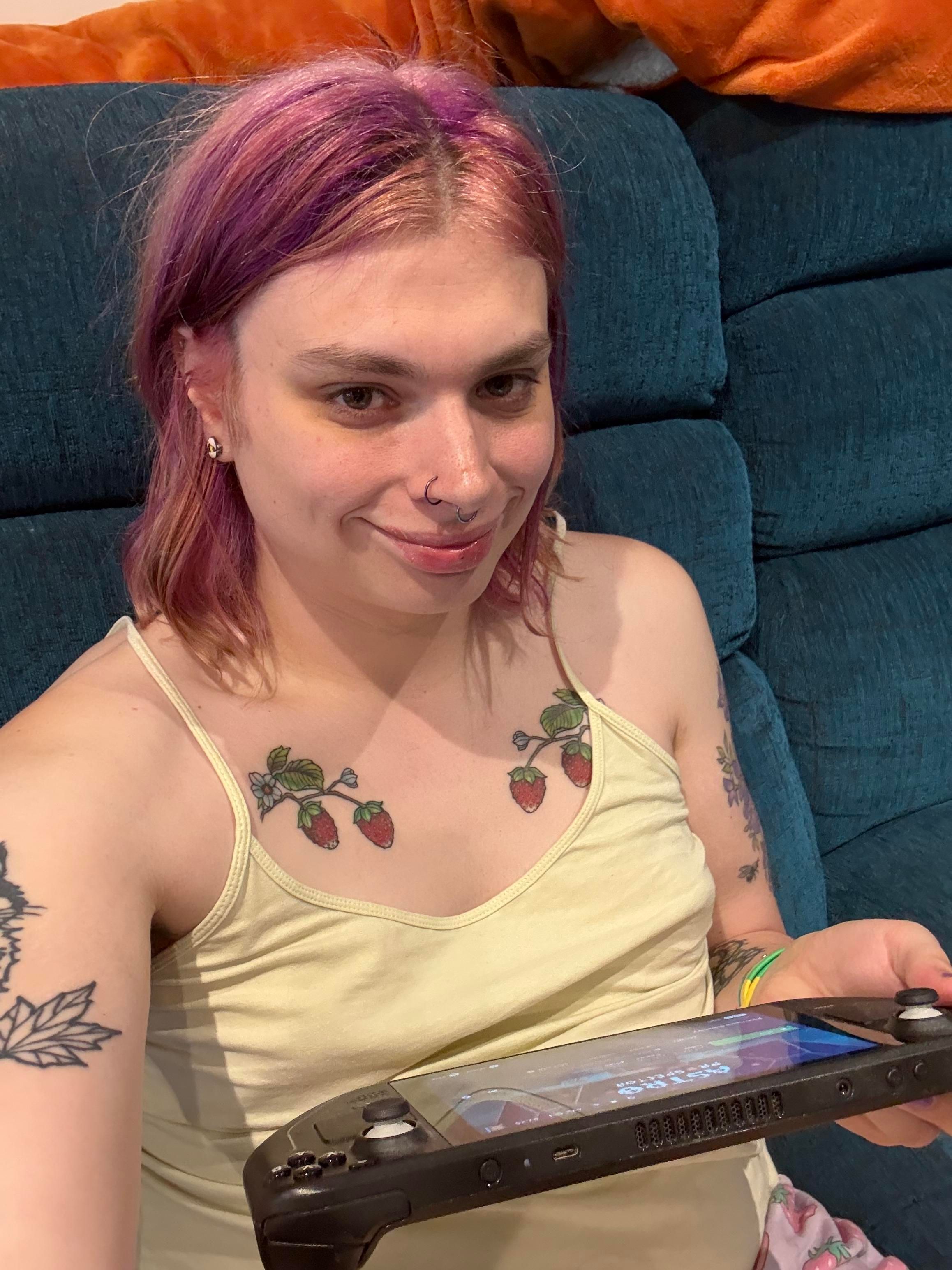 A selfie of Liv sitting on the sofa holding a steam deck. She’s wearing a yellow camisole top.