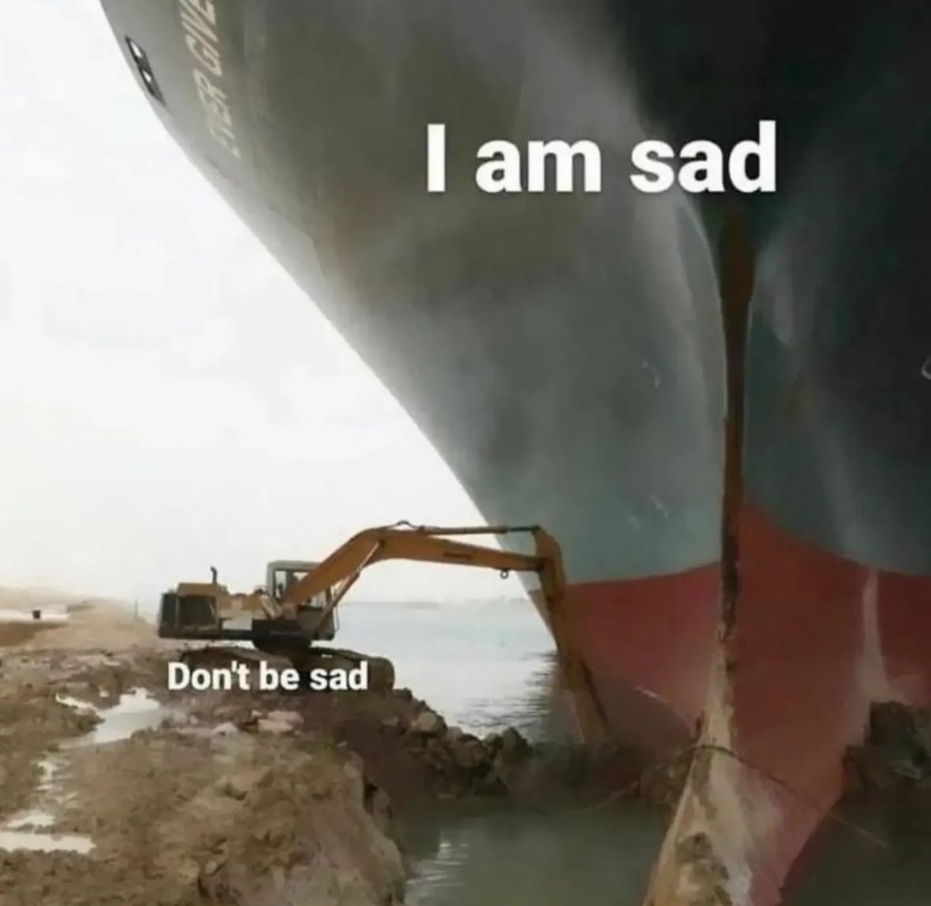 A meme showing the massive container ship Ever Given wedged in the Suez Canal with the text "I am sad" over it. A tiny excavator on the shore next to it has the text "Don't be sad" above it.