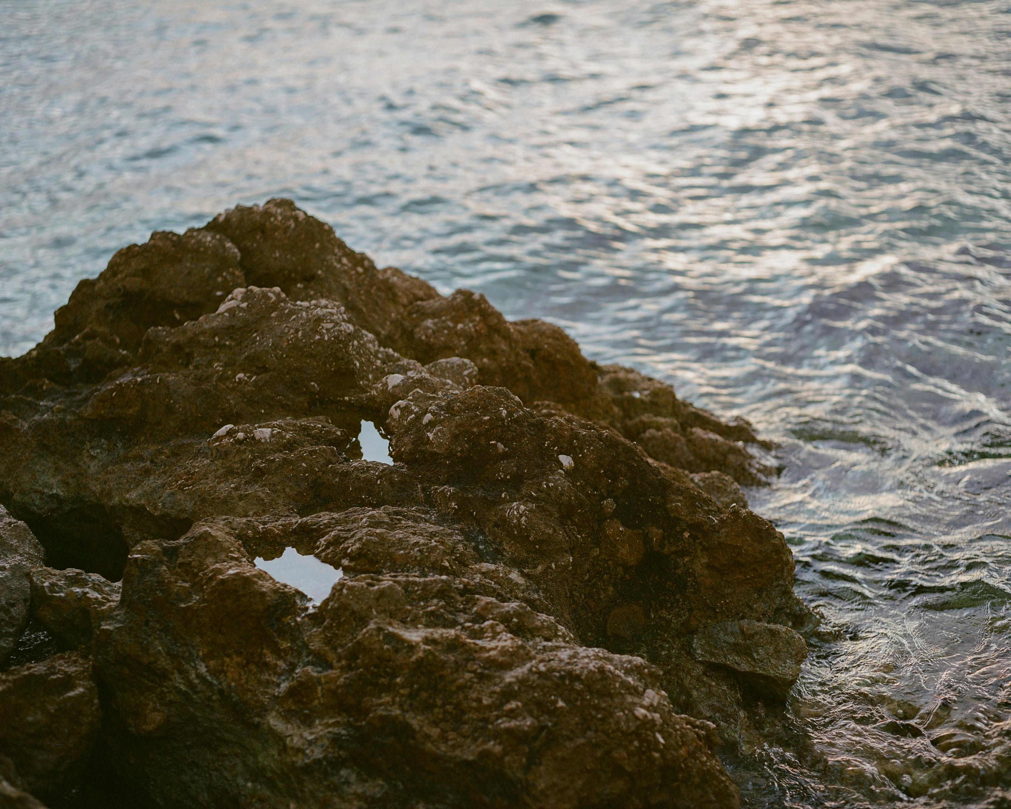 An eroded rock formation on the coast, with a few puddles brightly reflecting the evening sky; around, splashing Adriatic water.