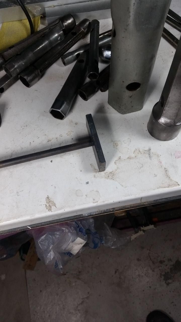 Pezzo di piattina in ferro, sezione 30×8 mm, lungo 70 mm, al quale è appoggiata una barra di tondino di ferro di diametro 10 mm.
Dietro un po' di chiavi a tubo.