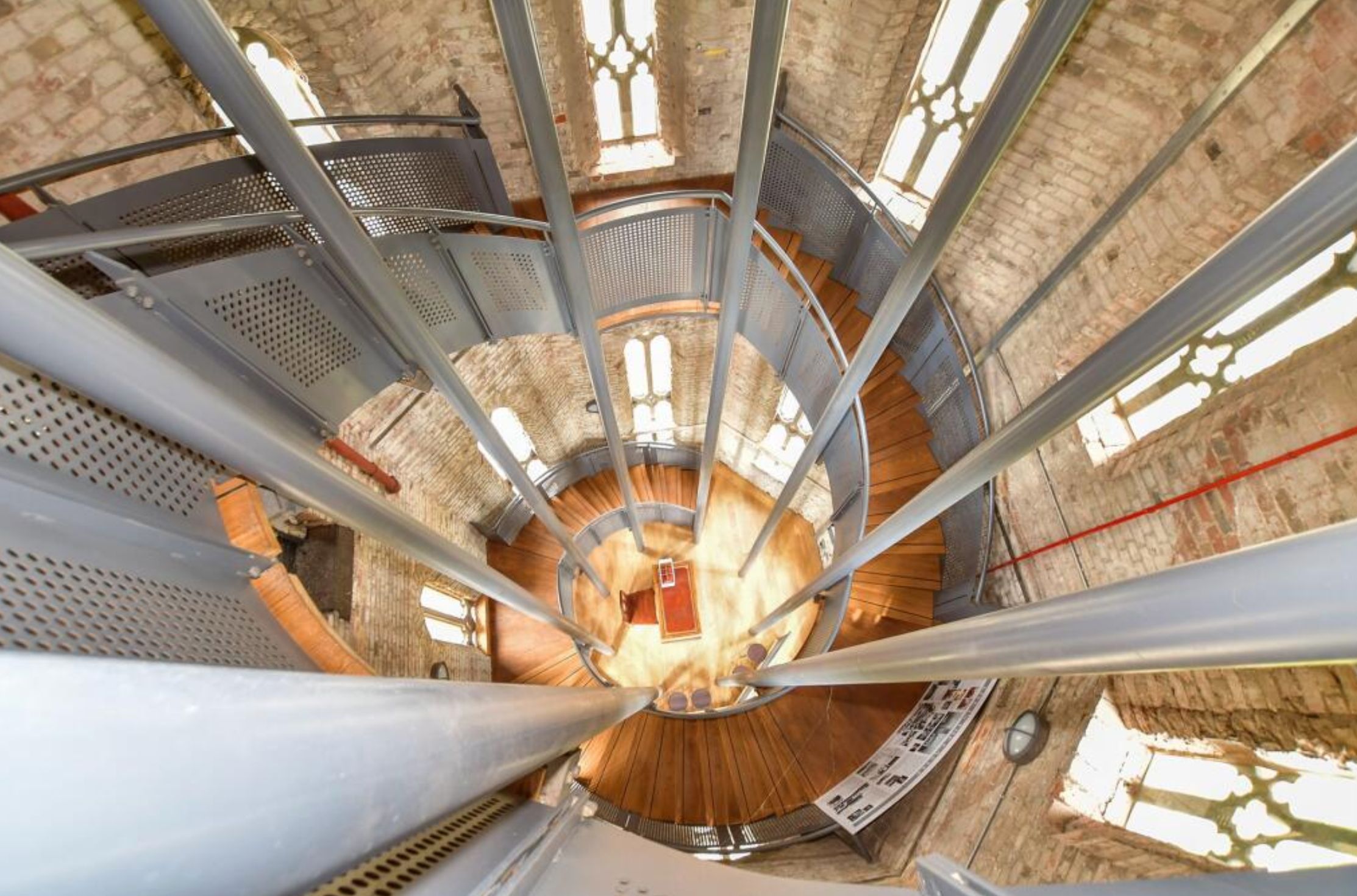An interior shot from an upper floor looking down into the central cavity of the building, and the stairs going around the perimeter. There are grey poles supporting the structure. 