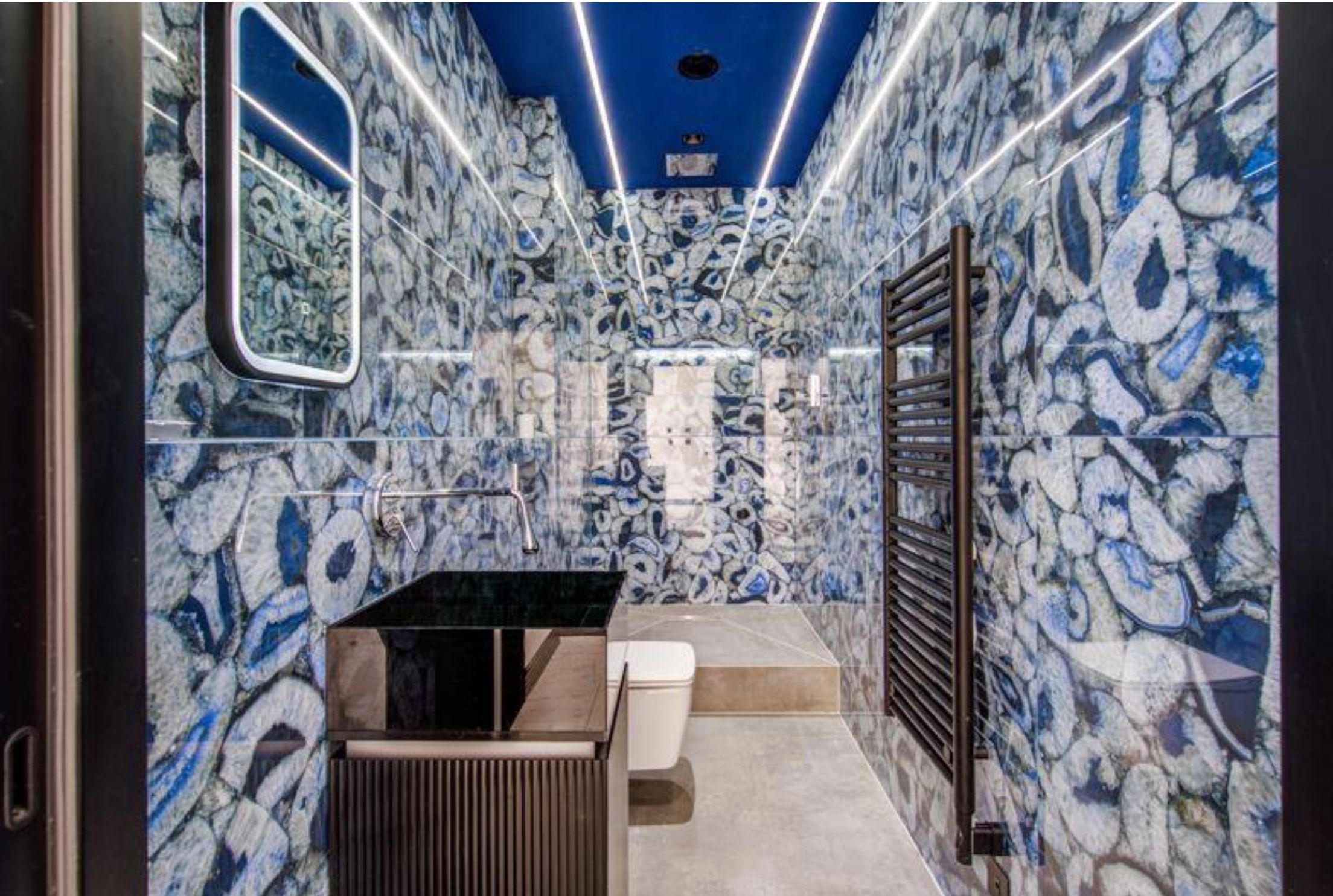 A bathroom that is entirely covered with swirly blue and white tiles and it reflects back so it looks a bit like it's an infinity bathroom, with strips of led lighting on the ceiling
