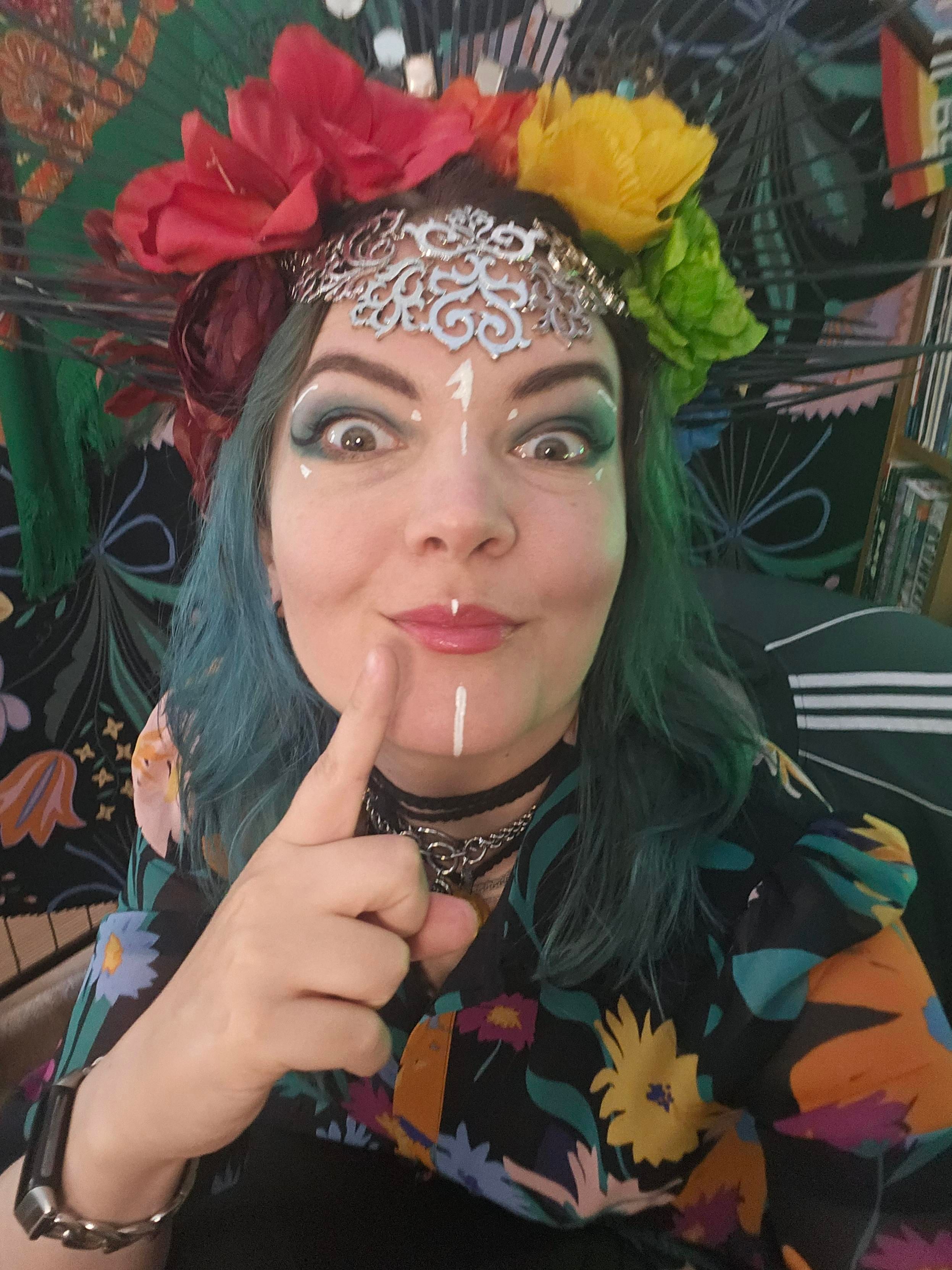 Selfie of a dressed up Jen with a flowery headdress and flowery dress. She is also wearing some facepaint and looking.... cheeky?