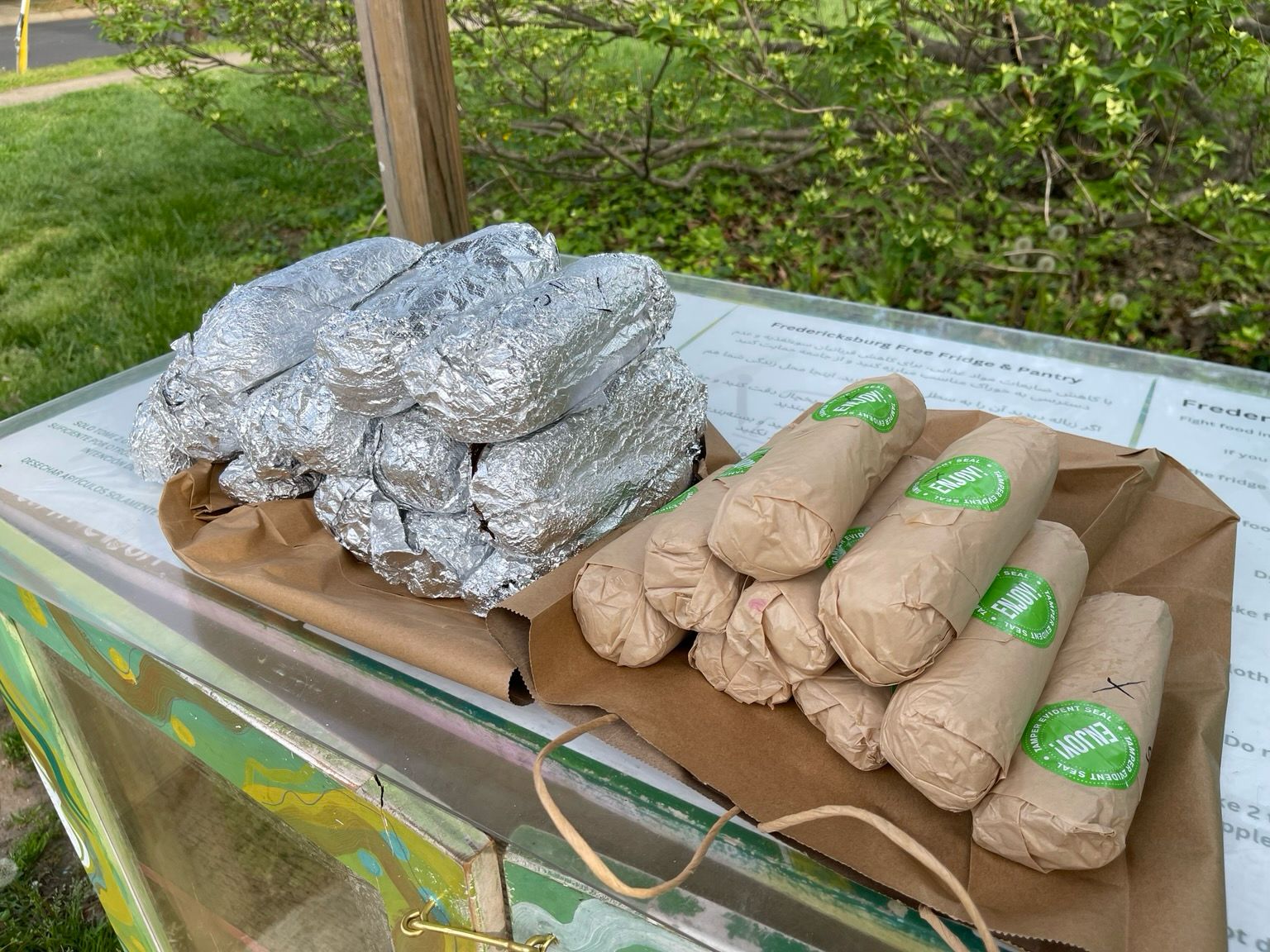 22 submarine sandwiches. Some in brown paper wraps, some in tin foil. A seal sticker says "Enjoy!". 