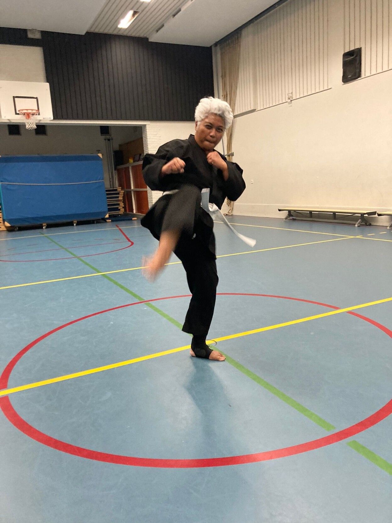 Black woman with gray hair in a black kung fu outfit with a white belt in a gym