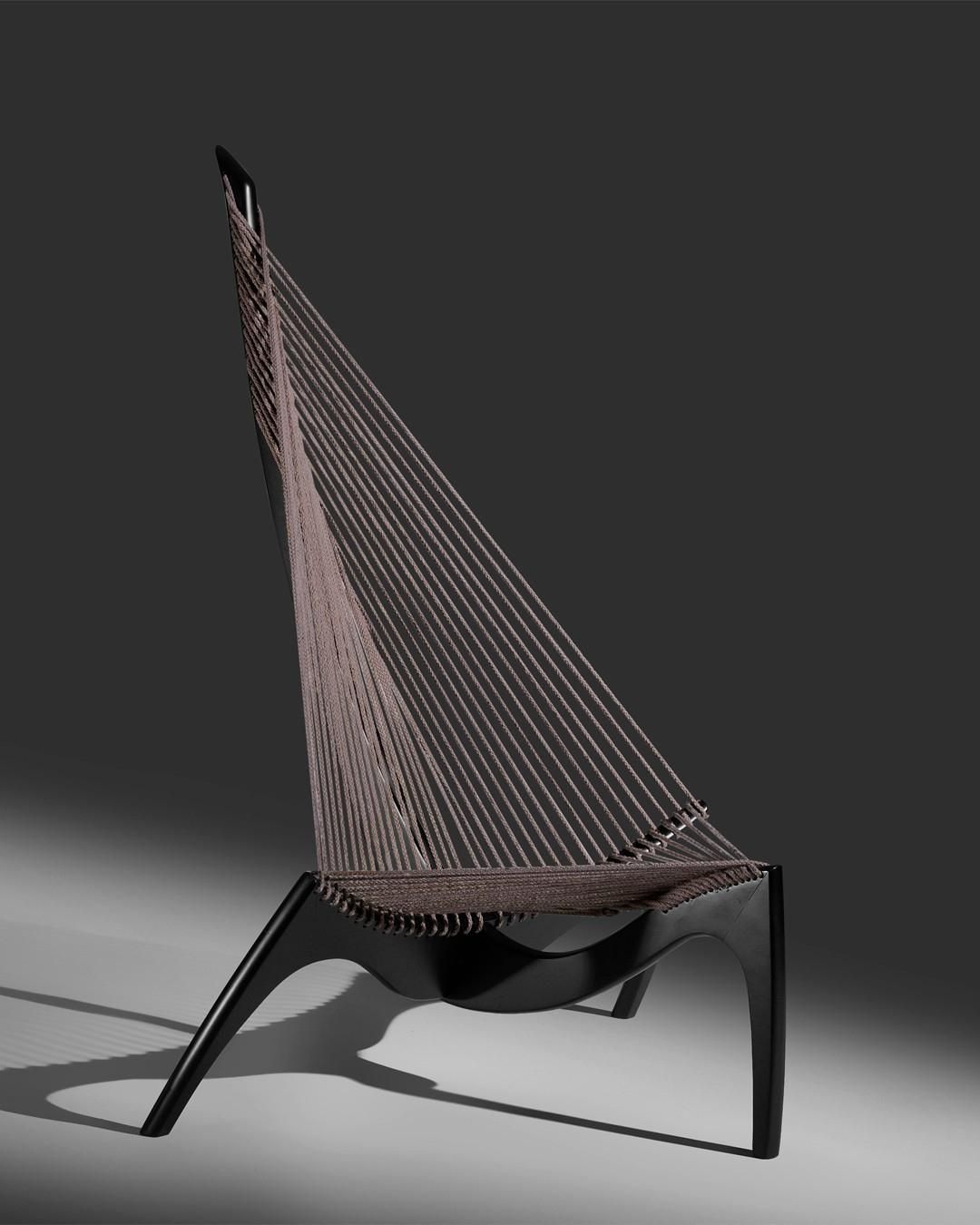 foto di una sedia di design che sembra un'arpa, con delle corde tese che partono da una base a 4 gambe in legno scuro di forma arrotondata e si legano a un sostegno verticale formando un triangolo.