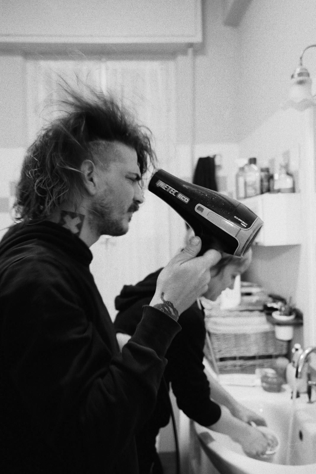 Black and white photo of a guy drying their hairs with a hairdryer.

