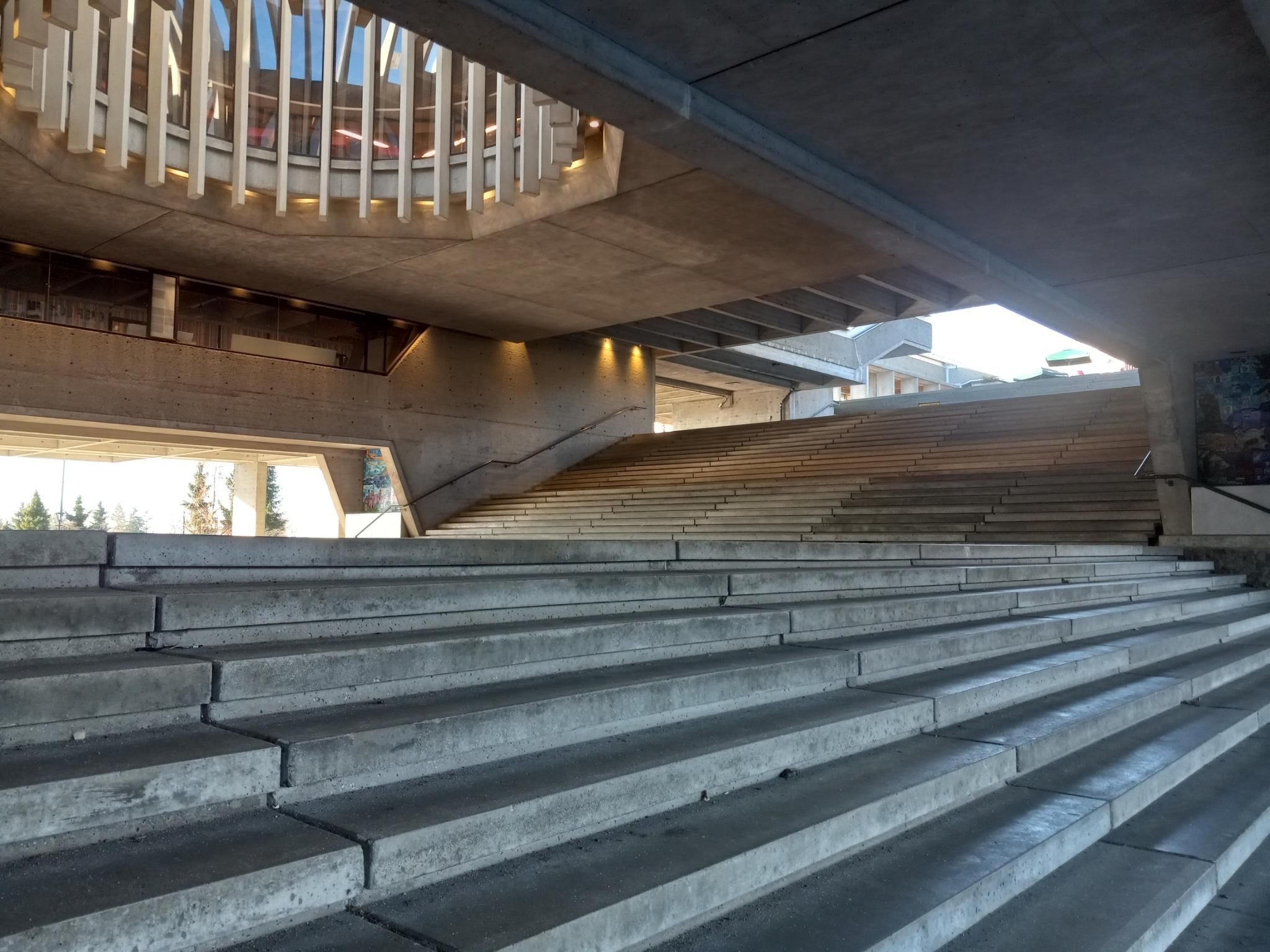 A view looking up a wide staircase that makes a 90 degree turn, and a weird round open space above it.  Everything is concrete and very geometric. 