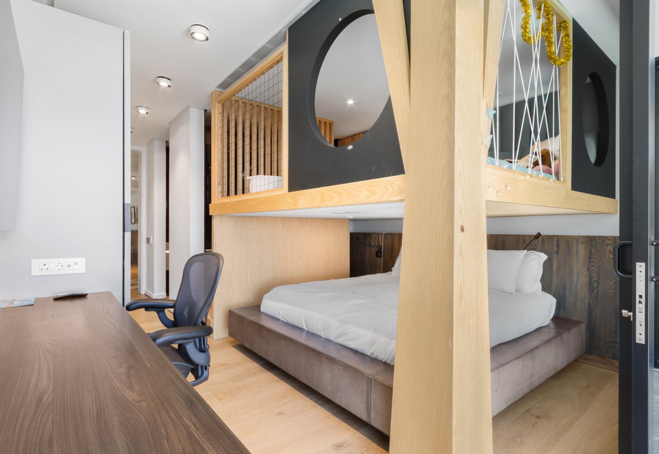 A bunk bed and there is no ladder to the top, and it's made of panels that have crisscrossed rope blocking it off, and the open panels have a circle in the middle of them. 