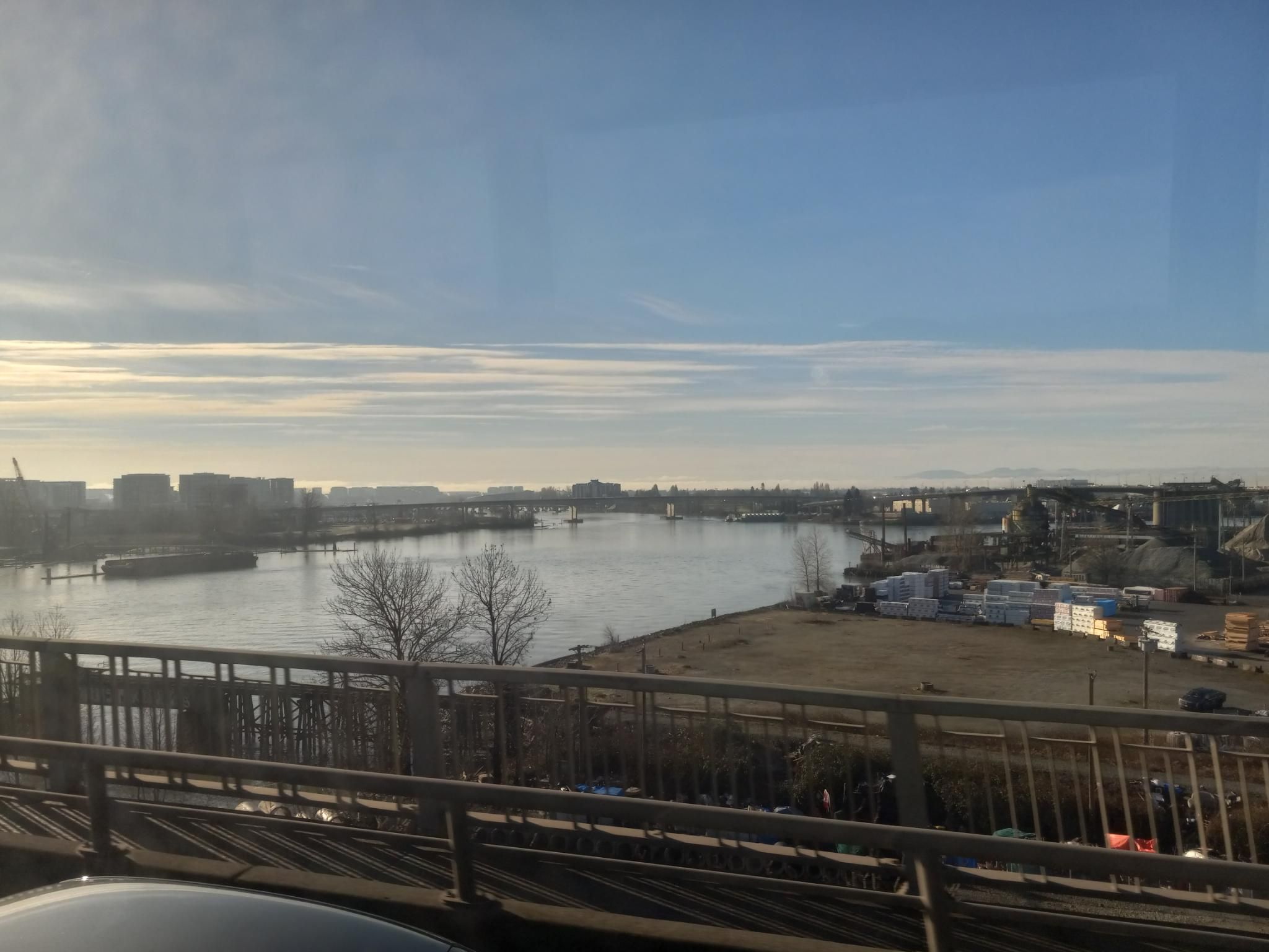 A view over the Fraser River from the Oak Street bridge.  There are lots of boats and semi-abandoned industrial areas on the sides of the river.  There's a little bit of fog, but mostly clear. 