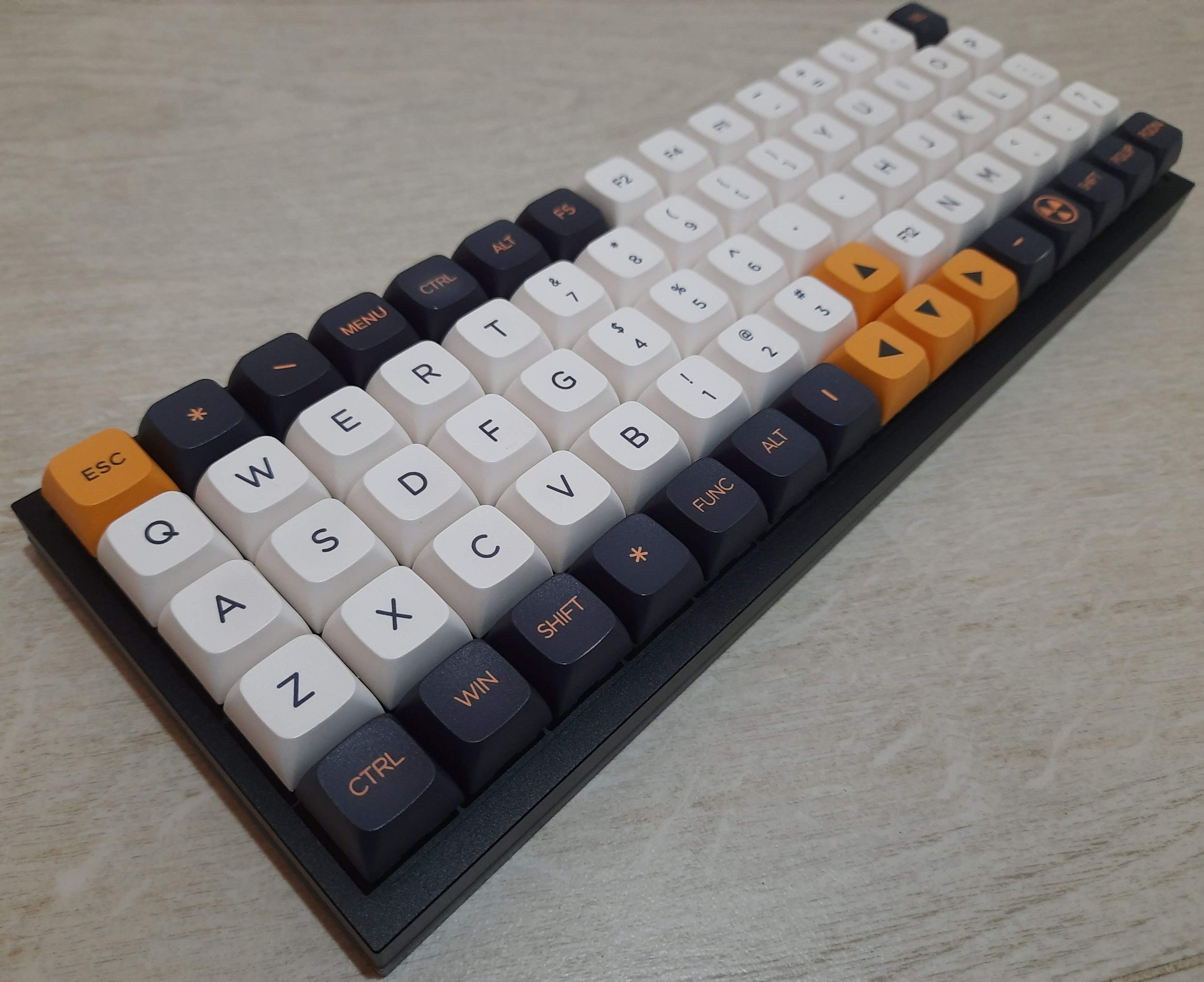 An ortholiner (also known as matrix style) keyboard, angled view from bottom left to top right. It has all 1U keys in a 15x5 grid arrangement, black anodized-aluminum case, and keycaps of three primary color variations: black on white for the alphabetic keys, black on orange for the arrow and esc keys, and orange on black for the other modifier and navigation keys. It shows a QWERTY layout split by a 5-key column. However, the actually typing uses Colemak layout by default.