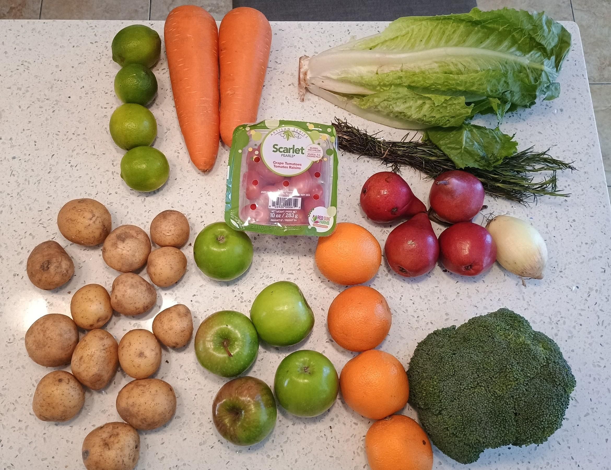 A bunch of veg and fruit includes limes, potatoes, green apples, red pears, carrots, lettuce, tomatoes, oranges and broccoli