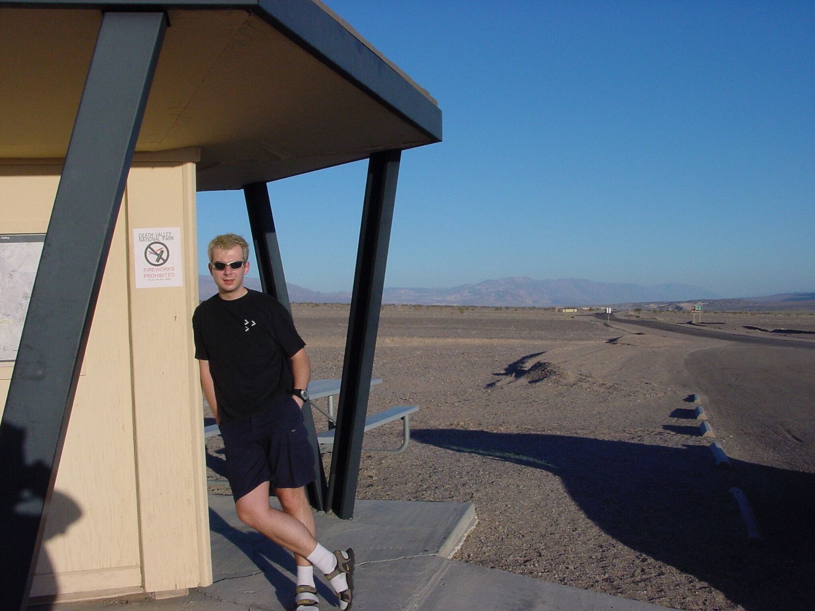 A young man leaning against small building in a desert landscape. Since that young man was me, let me paint the picture best I can: A black t-shirt and dark blue cargo pants. White socks and sandals. A plastic gadgety watch on the left wrist, it has a gray frame an a large white button. The sunglasses can best and kindest be described as very gadgety with their plastic, golden frames that are almost the opposite of what I should wear considering the shape of my face; they make my face head seem weirdly long. The fact that I was allowed to run around like that unstrained is proof that there is no such a thing as "fashion police", at least not when you need them. The only good thing about them is that they hide the piercing in my left eyebrow. 

And then there's the hair. My hair back then was a dark brown until the bleaching incident that made it the look on the photo. It's blonde-ish, leaning strongly on the yellow. It looks like the hair on those small trolls you put at the end of a pen as a kid, feels. Note that it is saved by professional and expensive intervention, since the (double) home bleach left it a very, very, very bright shade of orange. I have never since bleached or colored my hair.