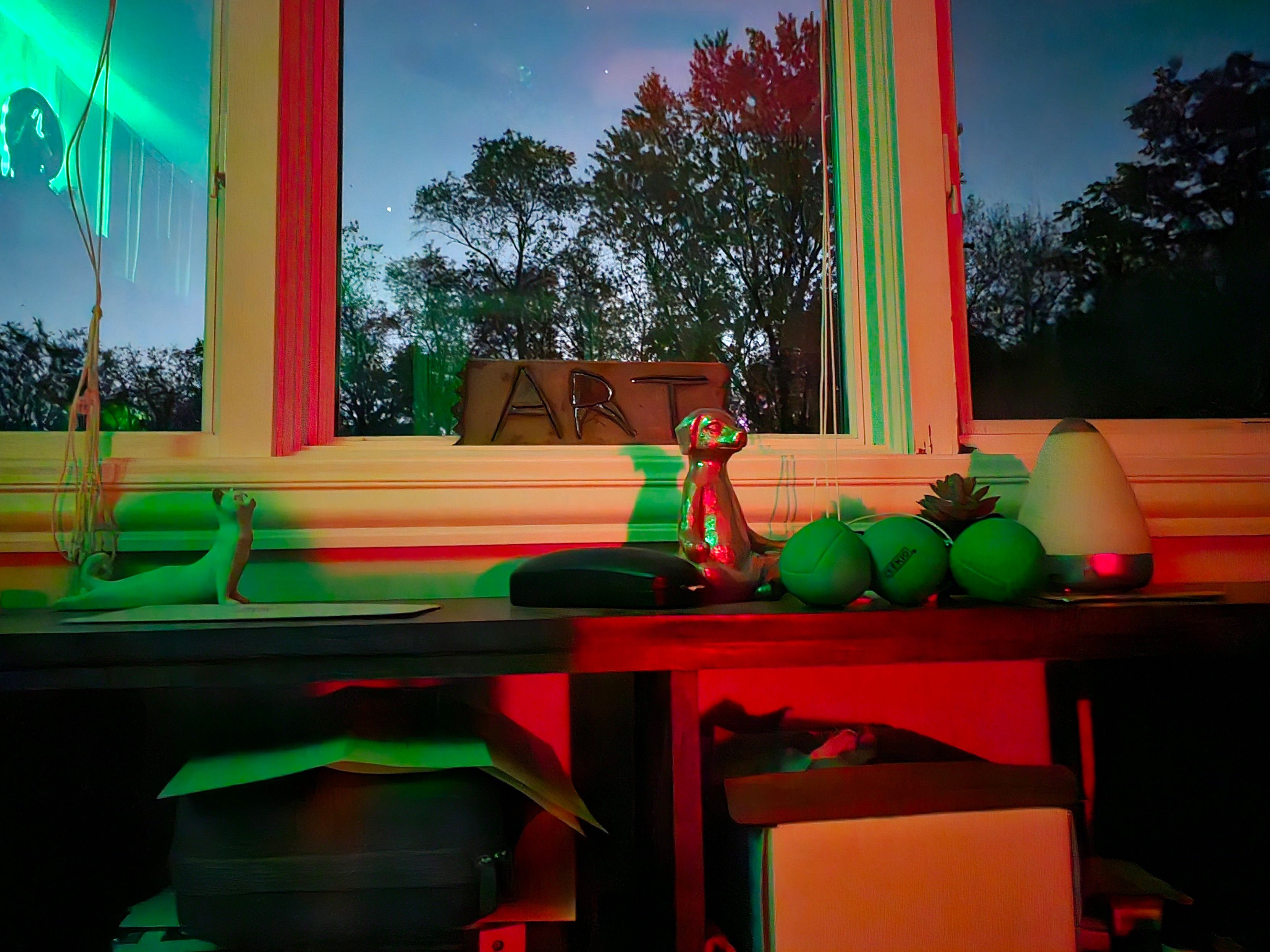 The moon backlighting a metal cutout of "art" propped in a windows, with a Buddha dog and yoga cat in foreground.