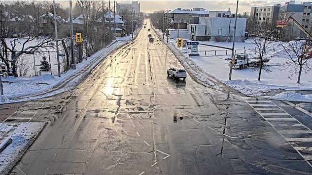 Looking along a mostly empty Carling avenue near Bronson, with the sun gleaming on the wet street with freshly fallen snow on the parkland to the left. 