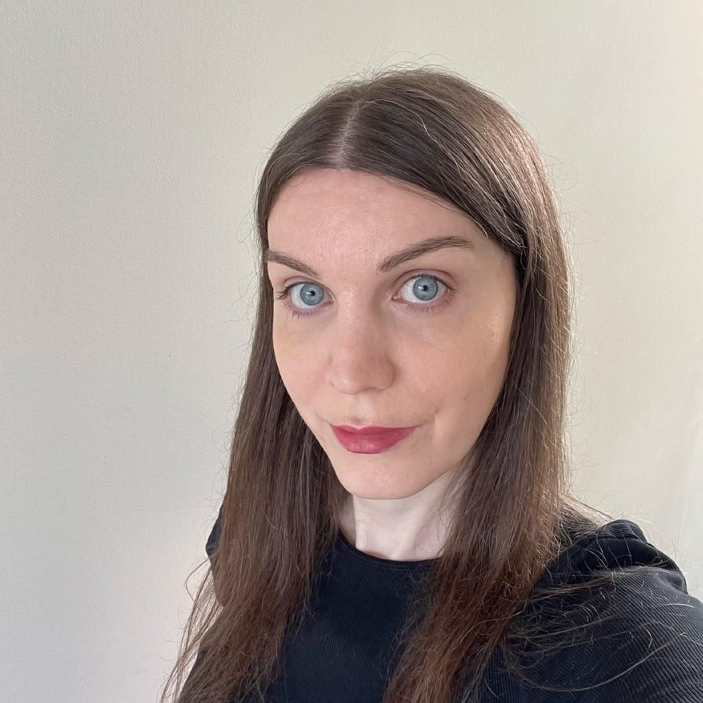 A photo of me, a 41-year-old white woman with blue eyes and long brown hair parted in the centre, wearing a black crewneck top