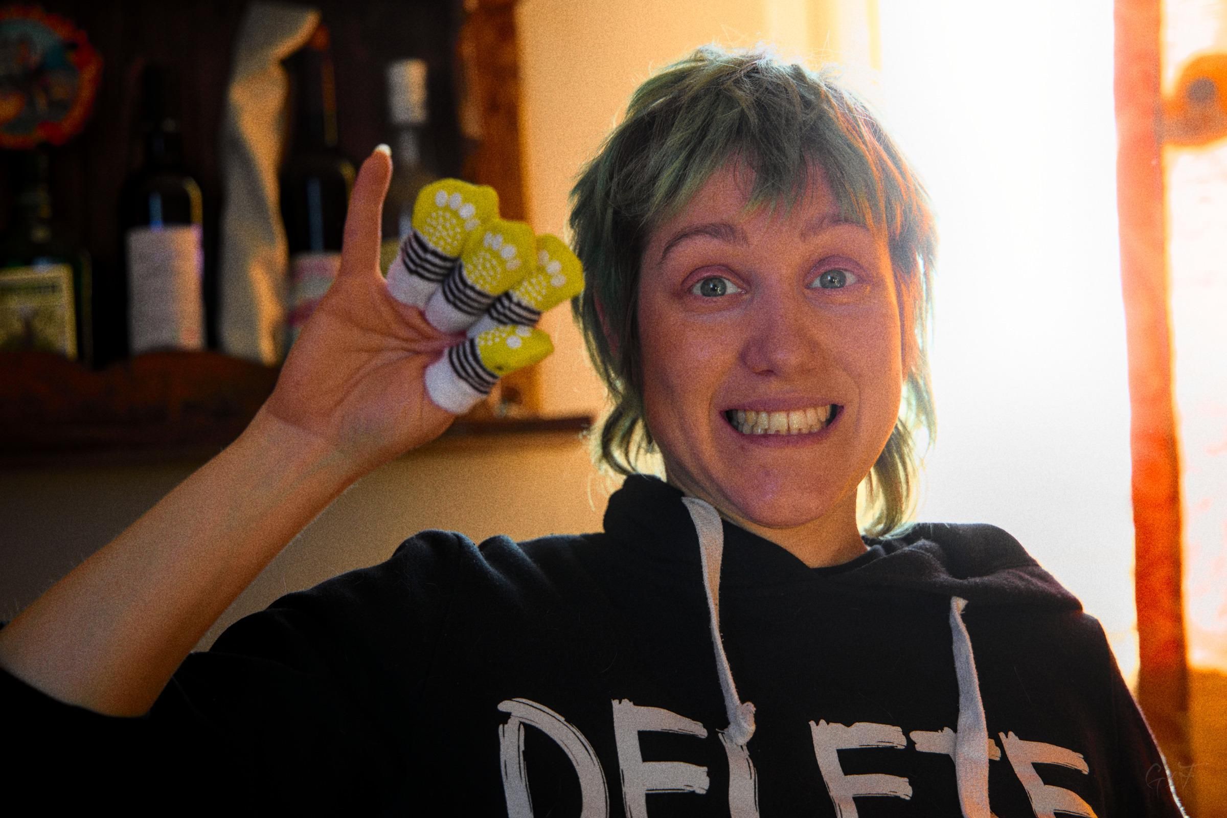 Photo of a woman, smiling and waving. She's wearing cat socks on her fingers.
