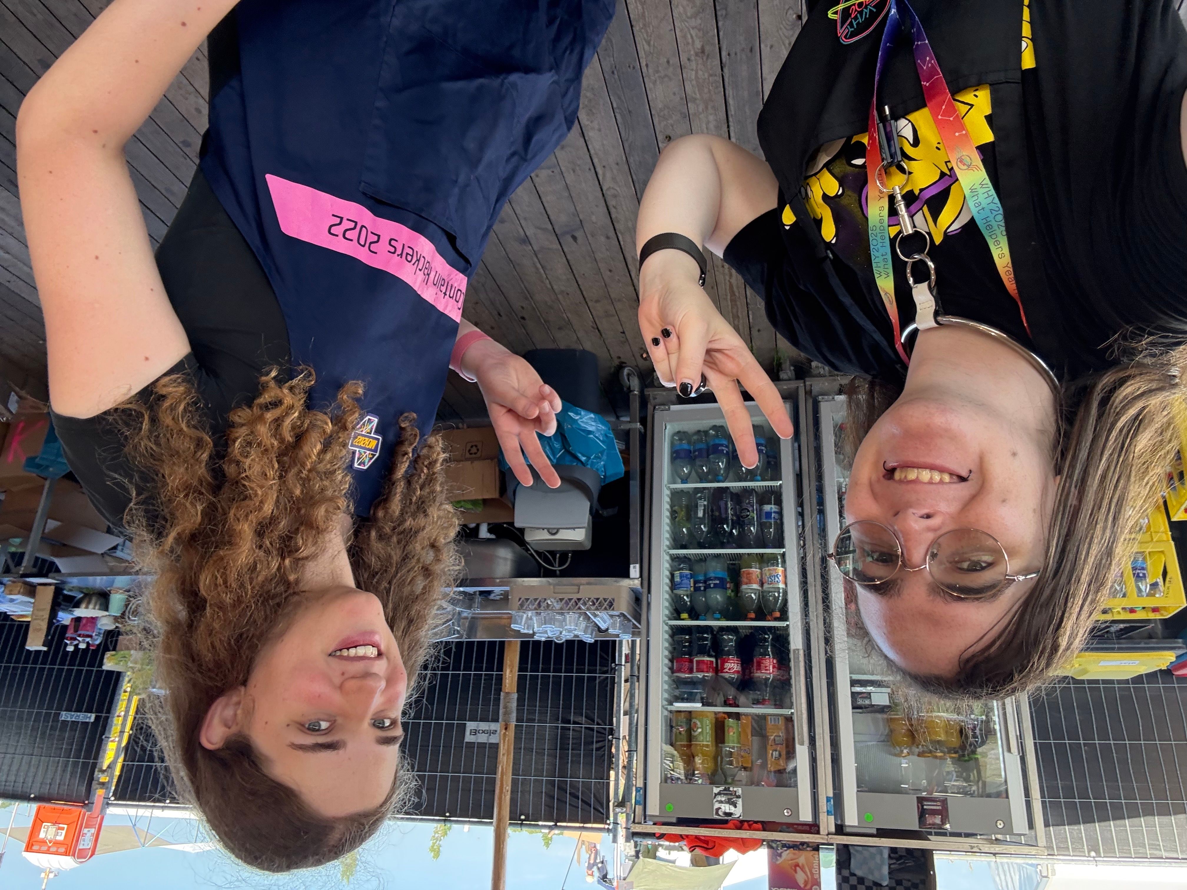 An eta and an unlobito grinning and making peace signs behind the WHY2025 main bar!