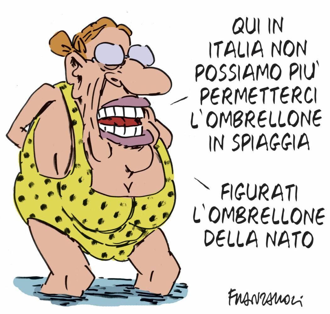 Nel disegno, una donna in costume da bagno commenta: "Qui in Italia non possiamo più permetterci l'ombrellone in spiaggia figurati l'ombrellone della NATO".