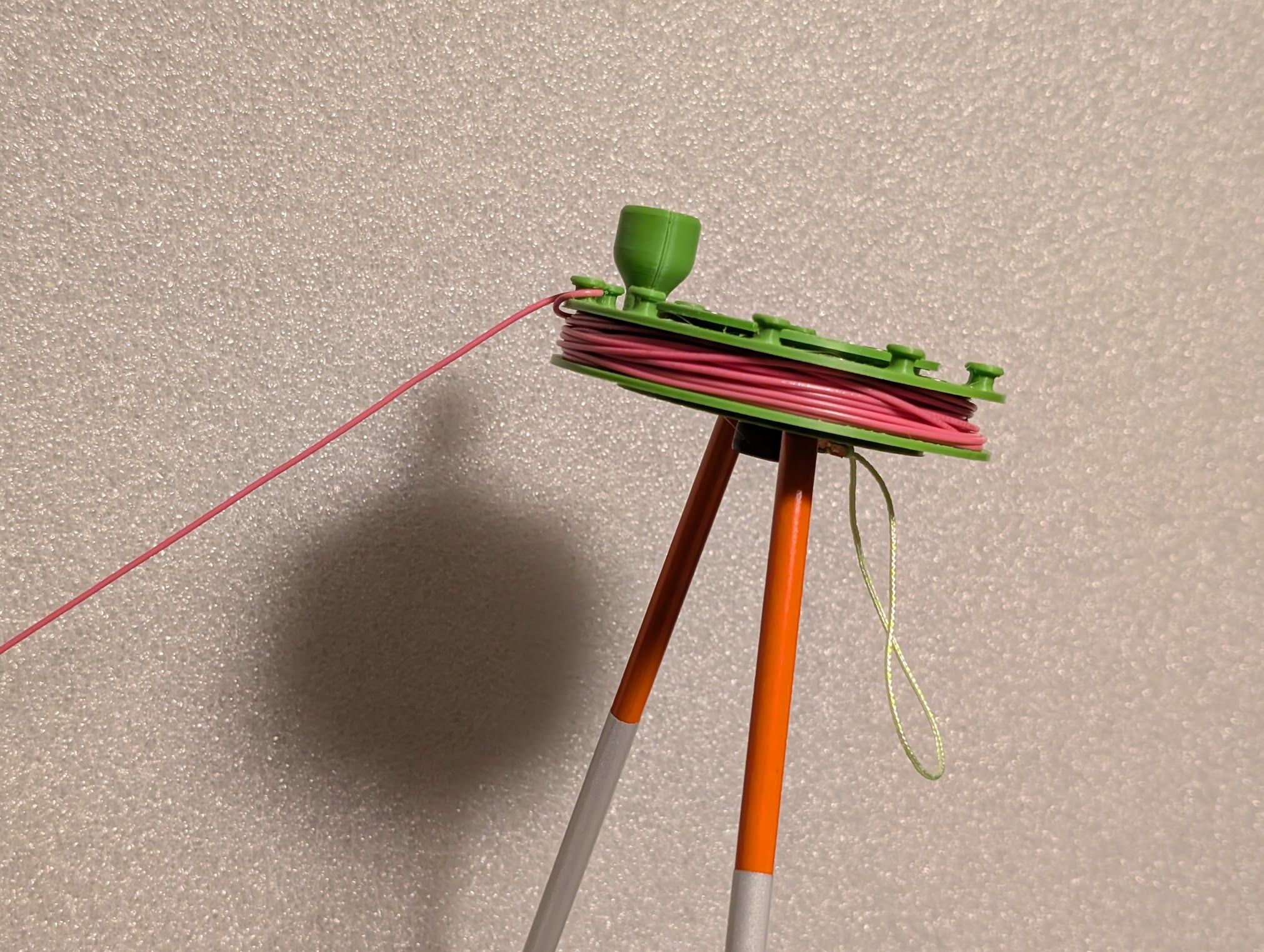 Photo of prototype showing spooled wire looped around stop knob, leaning against wire in tension. It stands on two fiberglass driveway markers as legs. A loop of cord hangs underneath for attaching a weight, but none is attached here.