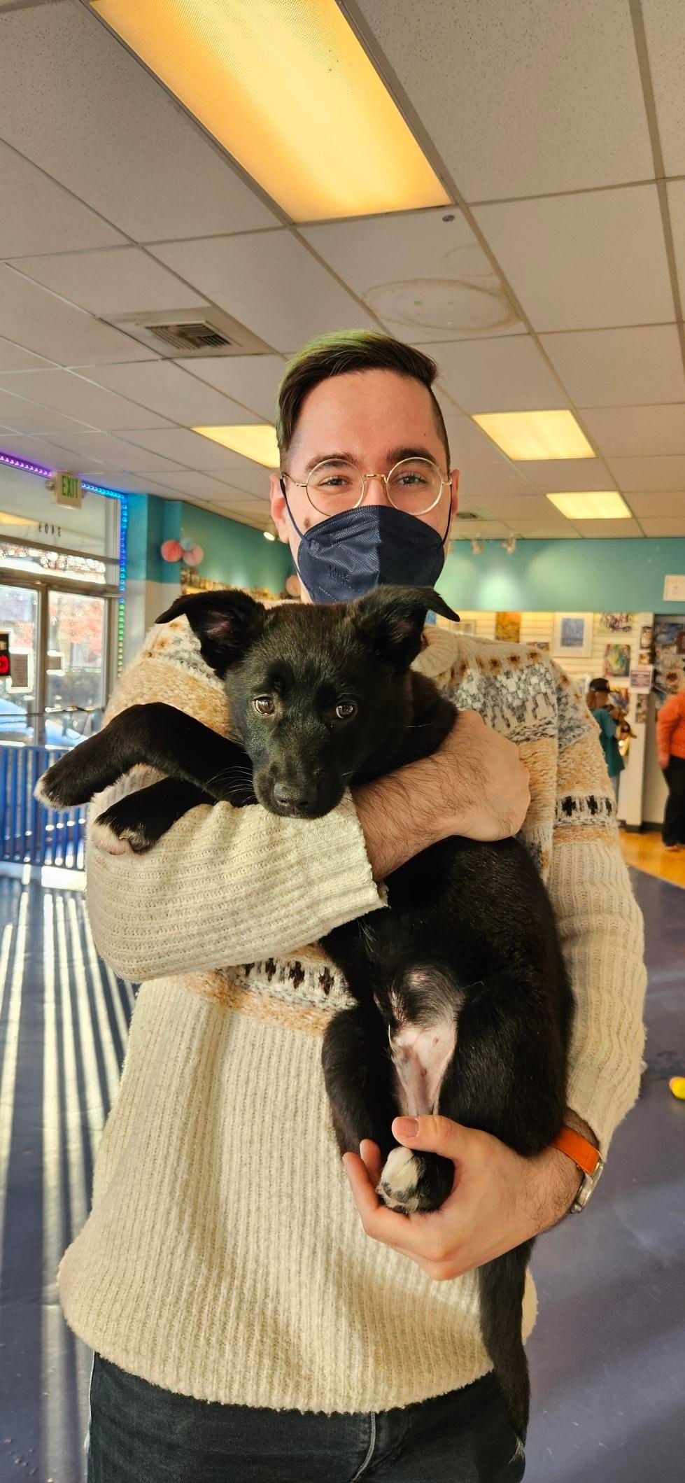 Me, wearing a blue mask, holding a black puppy in my arms. The puppy is very cute.