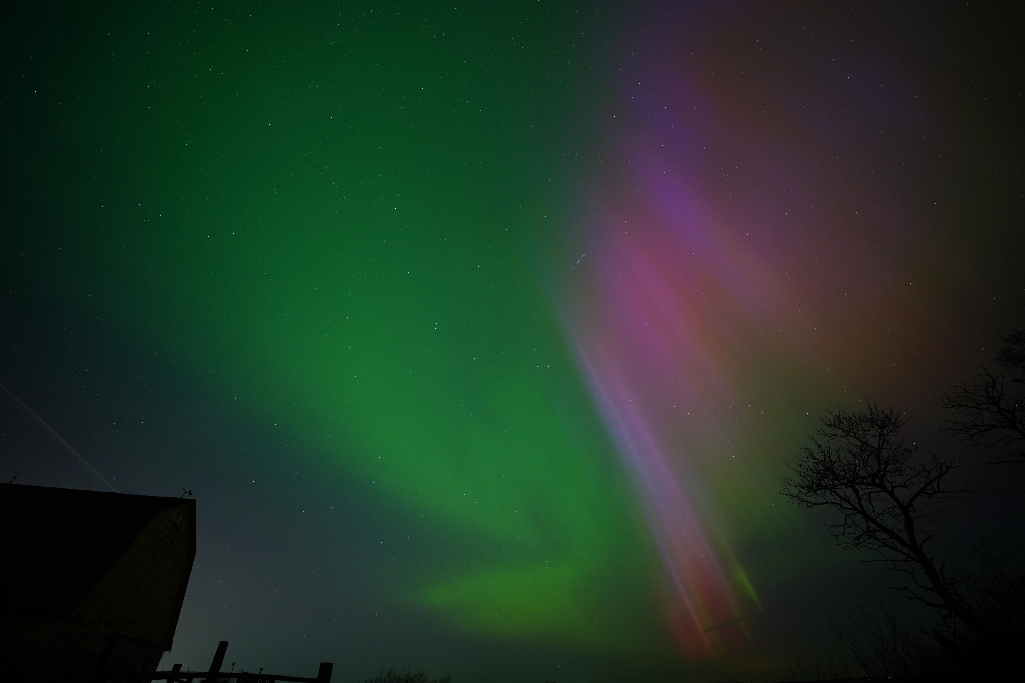 A patch of bright red and purple on one side of the sky, with bright green on the other, looking a bit swirly.  There's silhouetted trees in front of the red, and a silhouetted barn in front of the green.