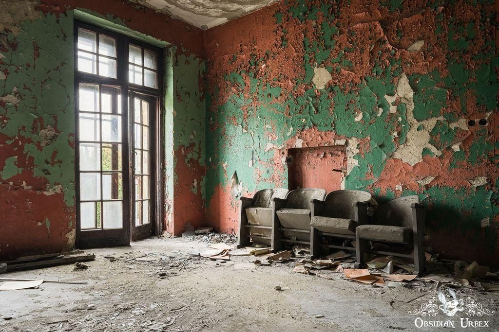 Abandoned room with peeling paint, four chairs sit against the wall.