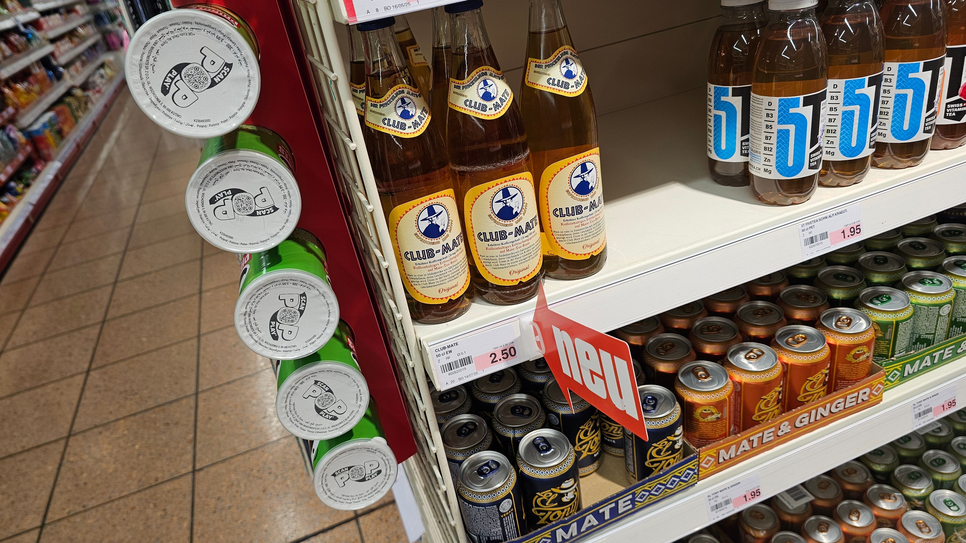 eine Handvoll Club Mate Flaschen in einem Supermarktregal mit einem Schild neu