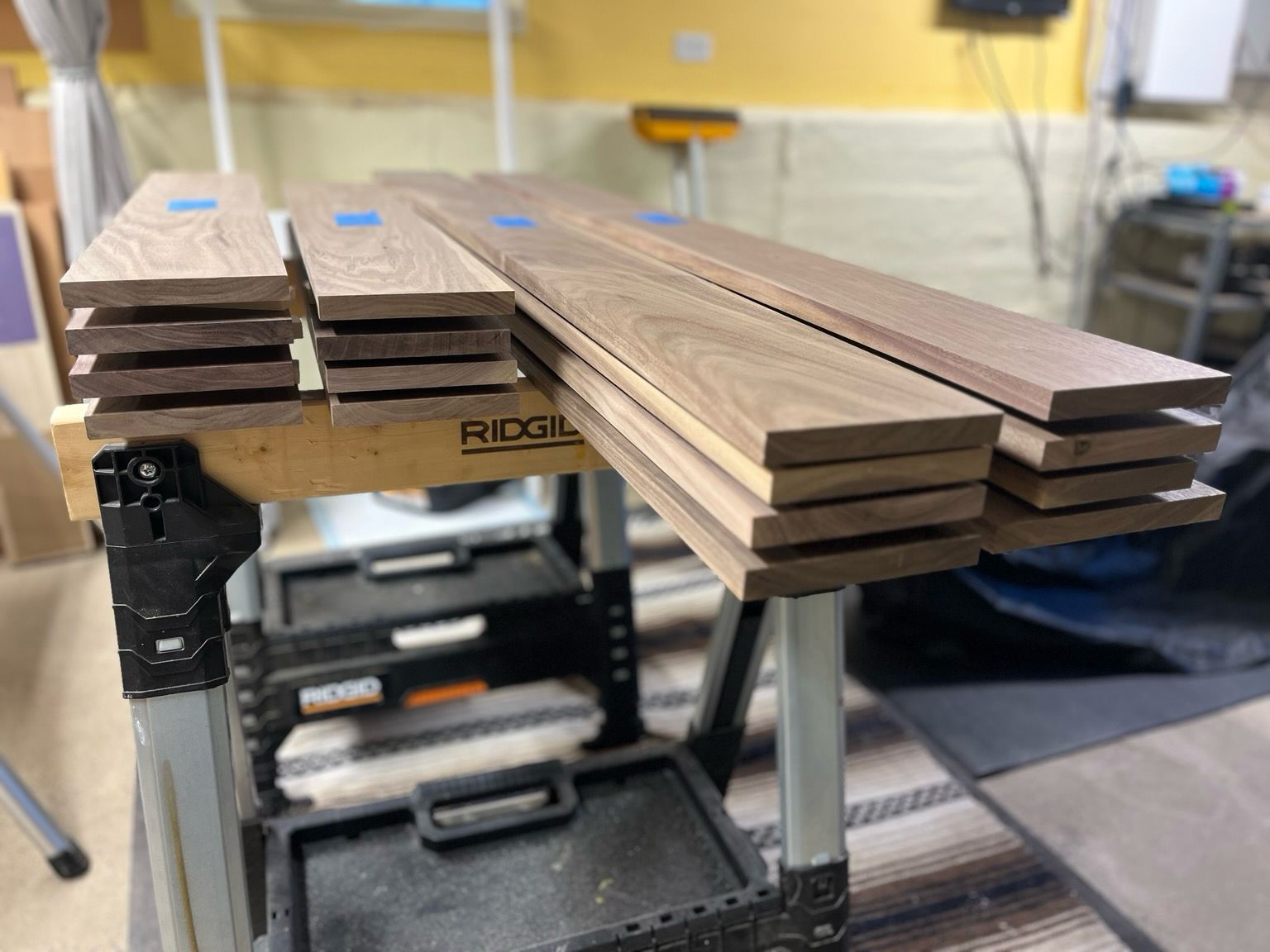 Four stacks of four boards of walnut on top of saw horses. 