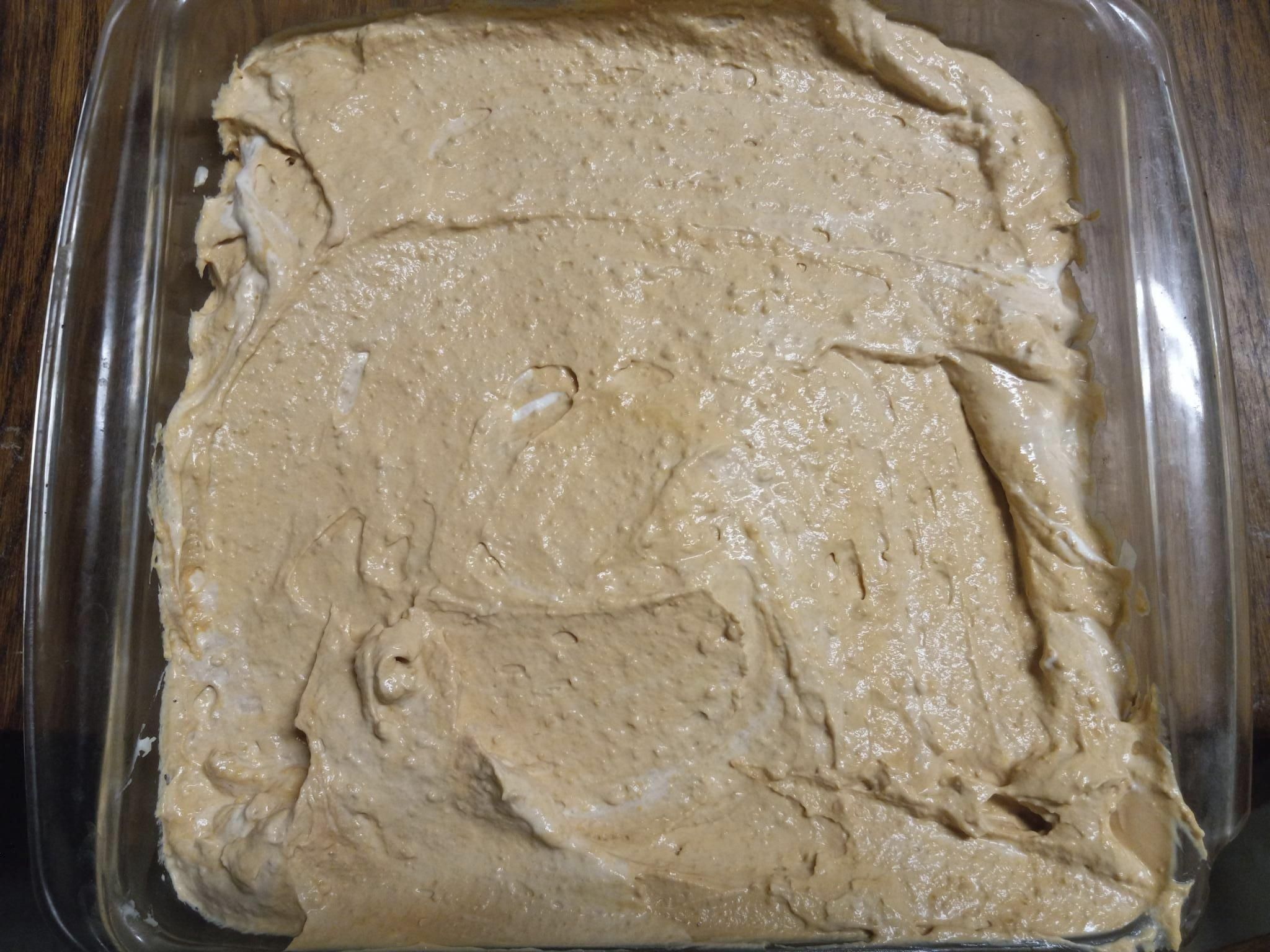 Looking down on a small, square glass pan that is full of caramel-coloured cheesecake.