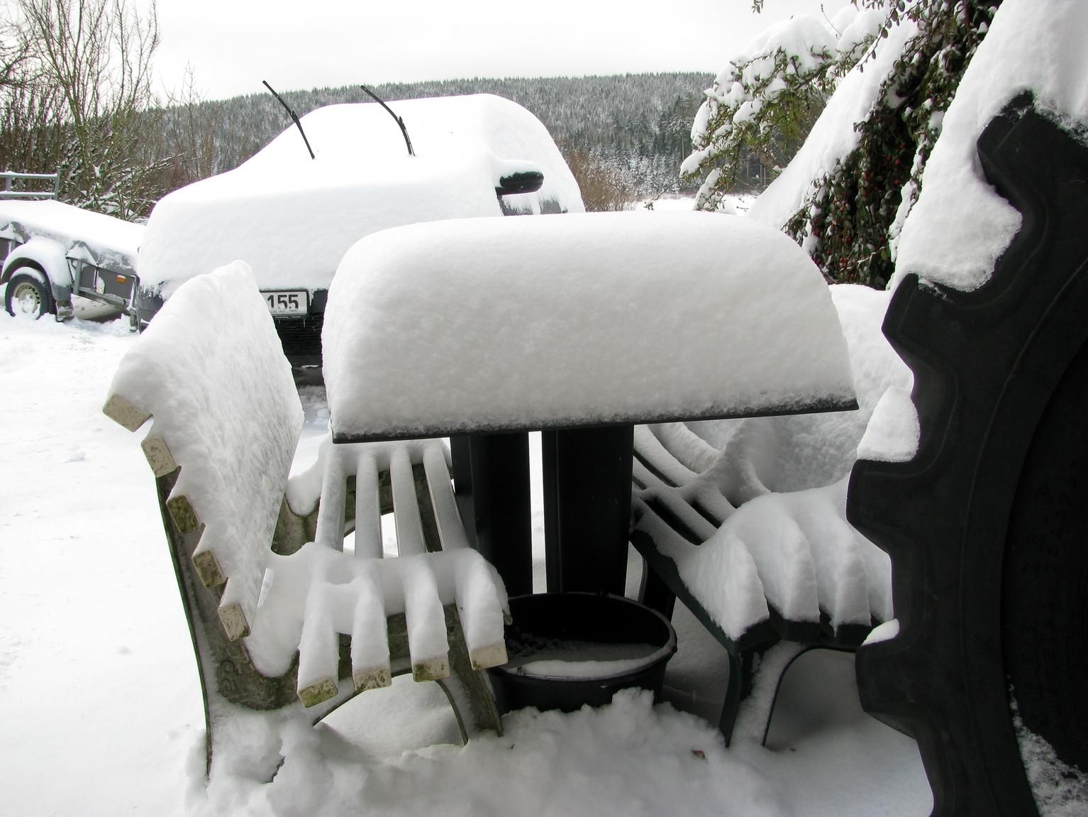 Schnee auf einem Gartentisch und auf unserem dahinter stehenden Auto.
