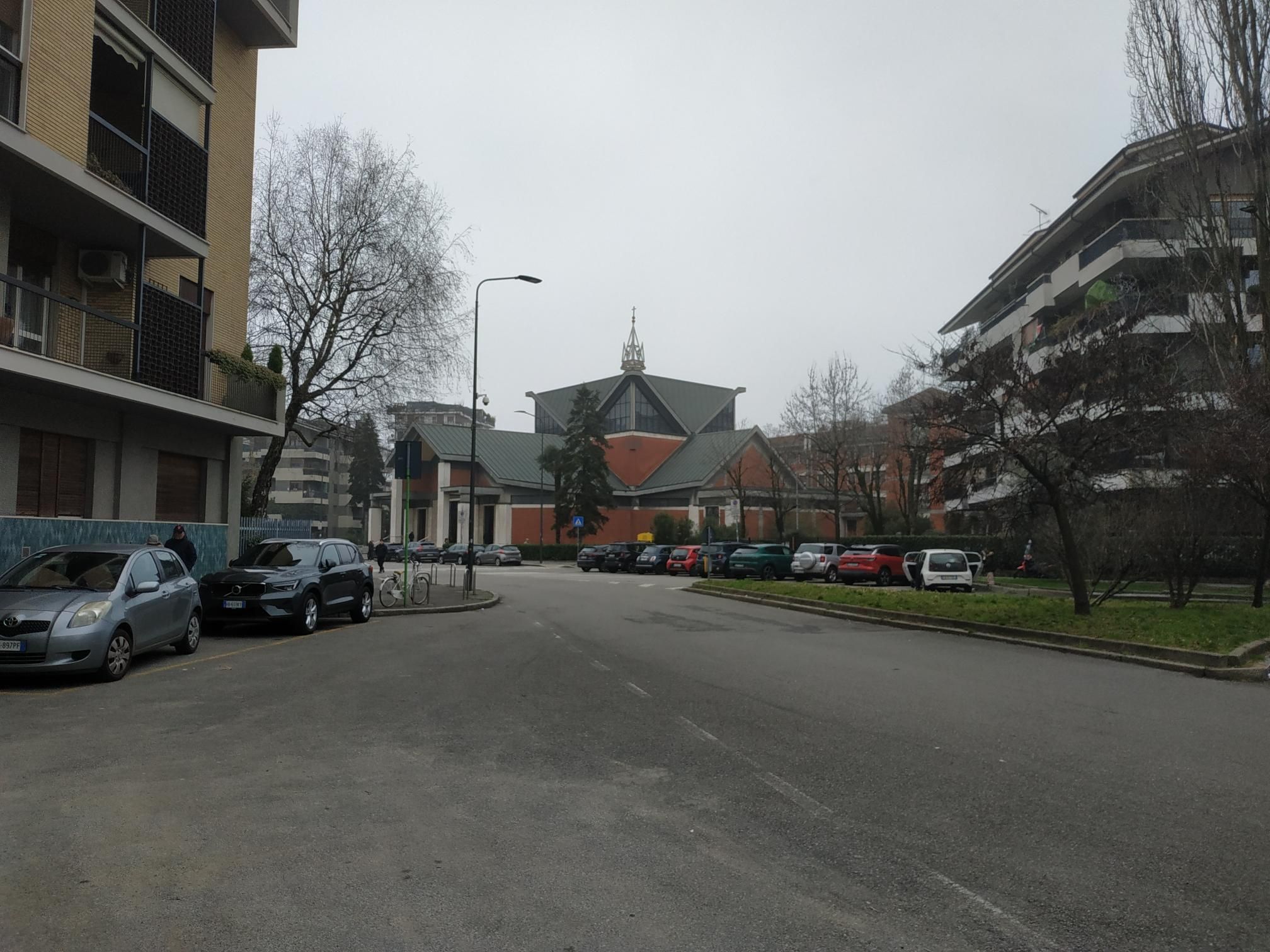 una chiesa rossa e grigia molto spigolosa. campanile sul tetto, molto appuntito e di metallo. attorno un ambiente residenziale cittadino.