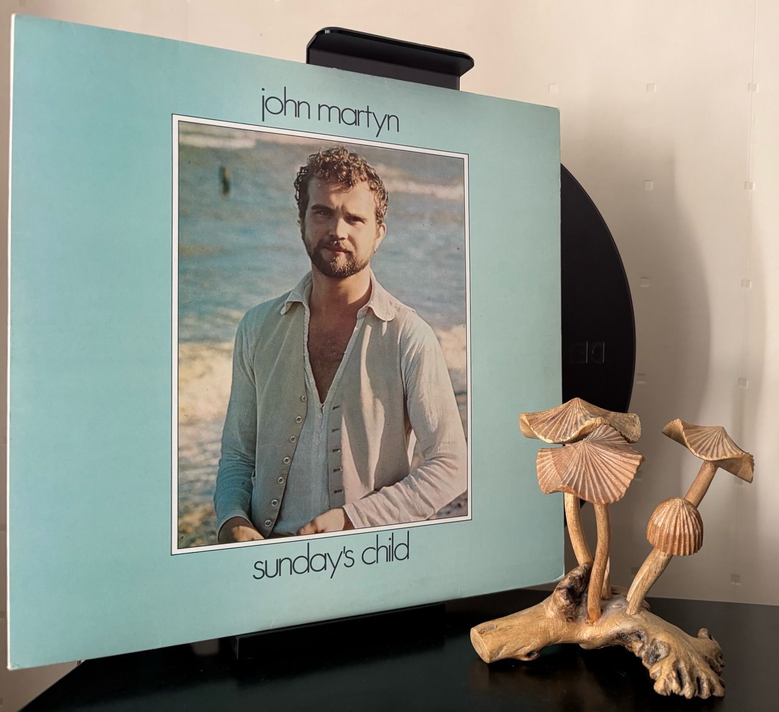 An aquatic coloured border frames the artist who’s standing in front of the sea. 