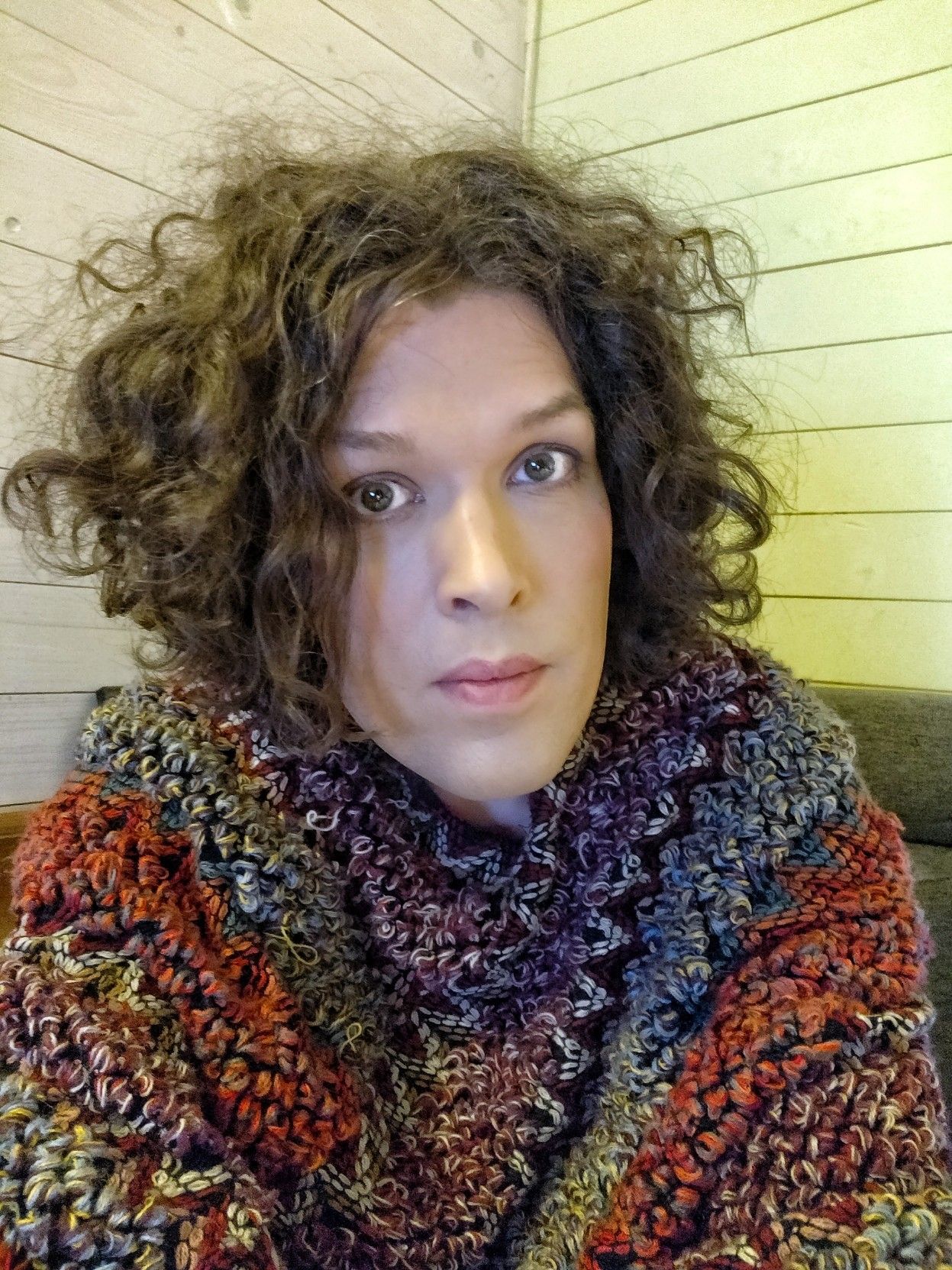 me looking into the camera with a serious expression, wearing a poncho on many colours, my hair is a mess