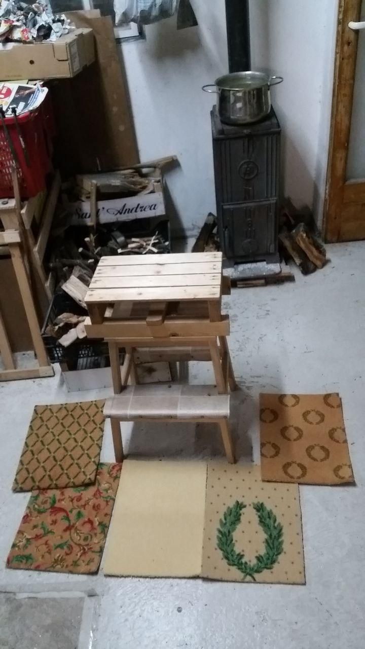 Sgabello Ikea Bekväm con sopra un semibancaletto di rialzo.
A terra 5 campioni di tappeto, uno in tinta unita (beige fluo) e altri con vari disegni.