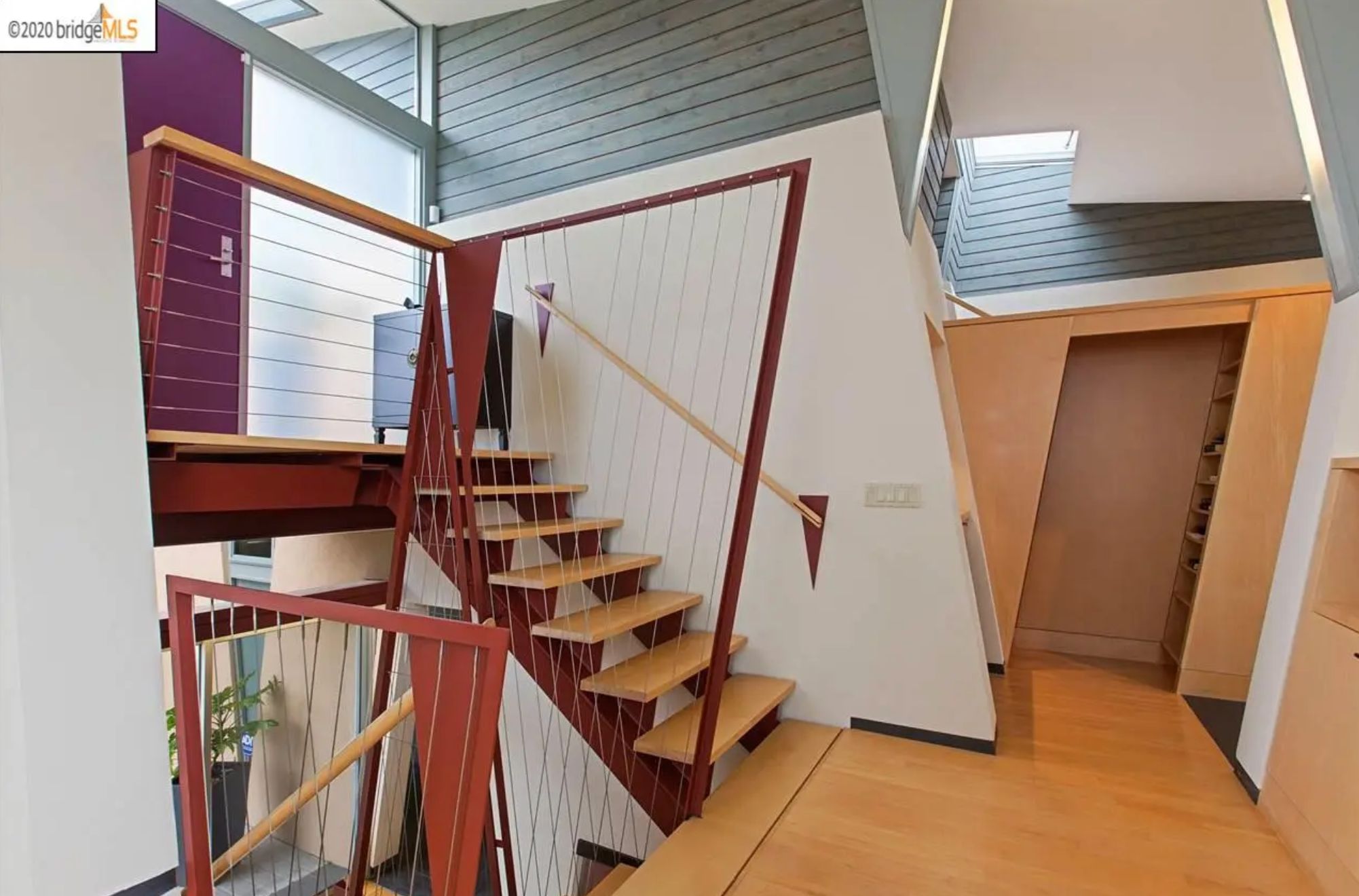 A stairway landing with a door that is on a slant. The wall on either side of the door is also on a slant, as is the railing for the stairs. 