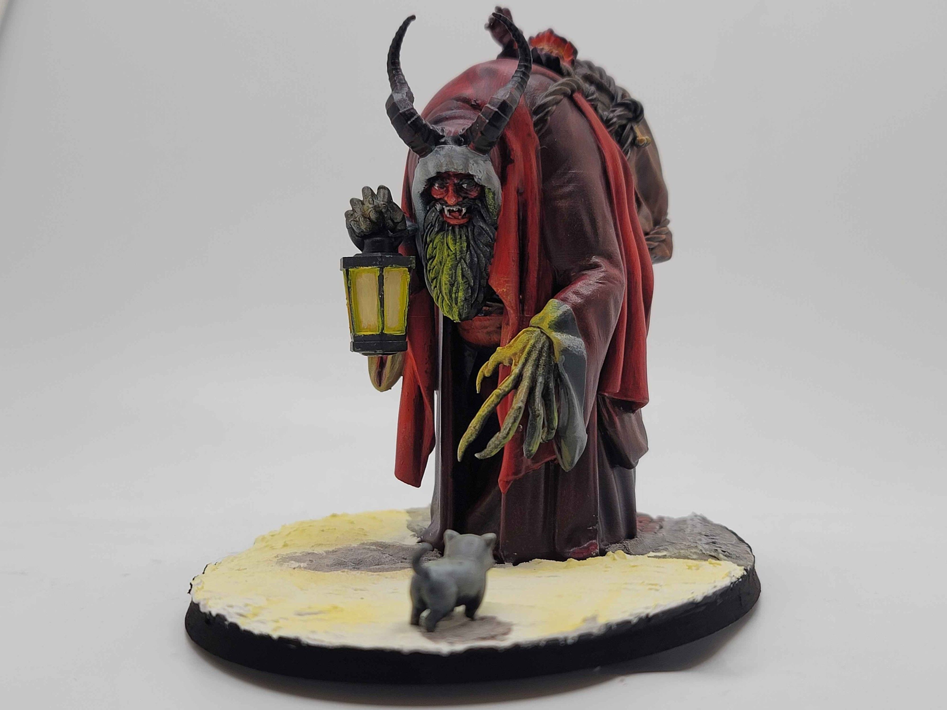 A miniature diorama featuring Krampus, Saint Nick's not so nice helper, facing off with an ornery cat (but I repeat myself).

The shot is from behind the cat, at a low angle, letting us see Krampus's devil face beneath his hood.  The cat is white, and so the shadows and yellow lighting make it mostly grey or yellowish.  

The base of the miniature is an oval, with the cat at the extreme of one end, and Krampus just on the other side of the center line, with most of the base covered in snow, which is either in shadow from Krampus, the cat, or the bottom of the lantern, or lit yellow by the lantern's light.  Krampus's beard is half yellow from the lantern, as is much of his left thumb and forefinger, with all fingers monstrously elongated.  Between his horns, reaching out of the bag on his back, is the arm of a small child, prevented from escaping by a thick rope across the mouth of the bag.

Krampus's robes are dark purple in the shadows, purplish crimson for the underrobe, and bright Santa scarlet for the overrobe, with white cuffs around the hood and wrists, while the bag is variegated shades of brown, wrapped with brown rope, the knots holding the web of ropes together bound in place with bones. 

In his right hand, Krampus holds an iron lantern, dark except for the bright yellow light pouring from inside, and his great horns are black with red highlights.  His face, beneath the hood, is a shadowy red, with just the tip of his nose, peeking out of the shadows, pale flesh.