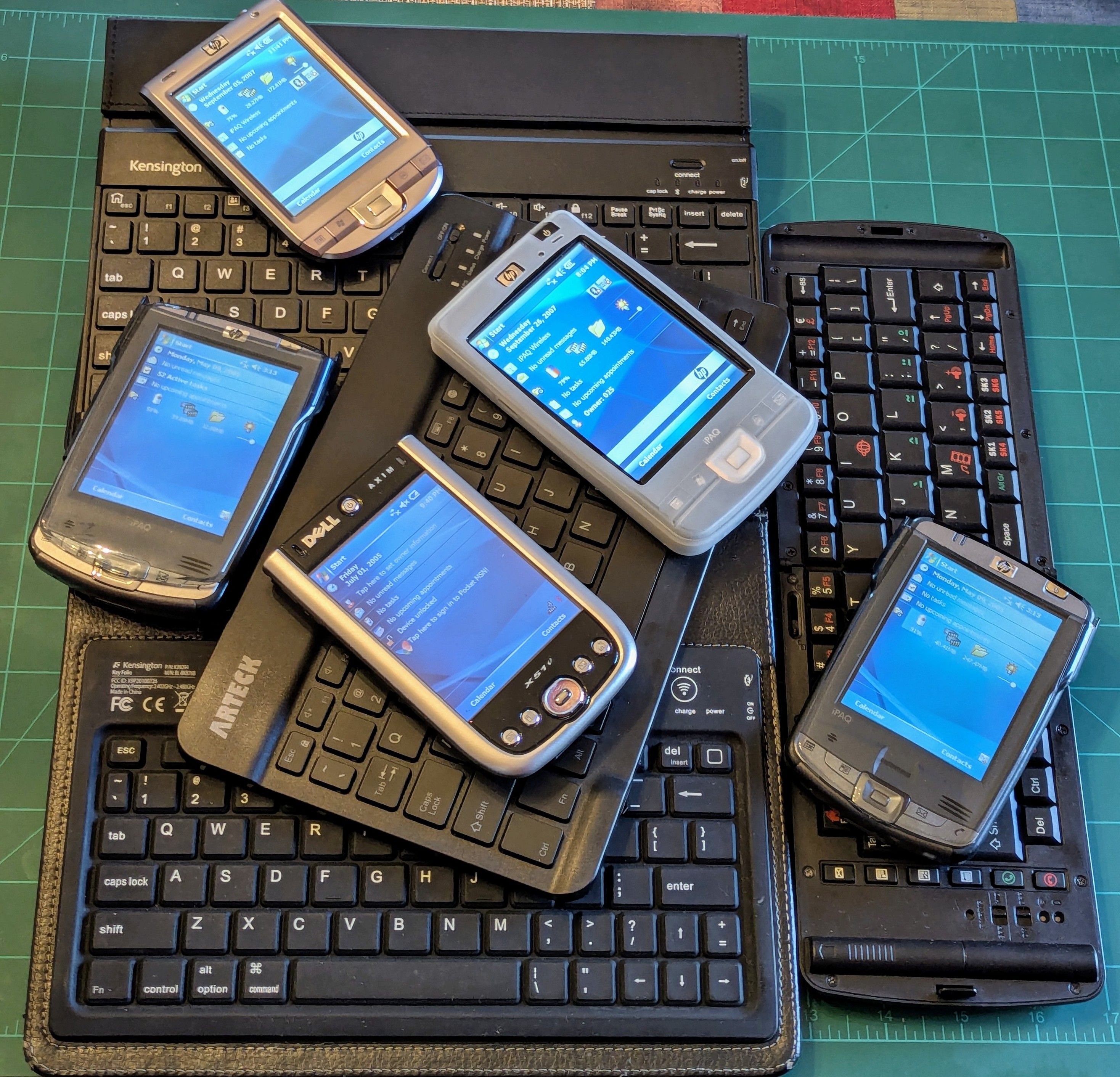 A pile of Bluetooth keyboards with various iPaq and Axim Pocket PCs laying on top.
